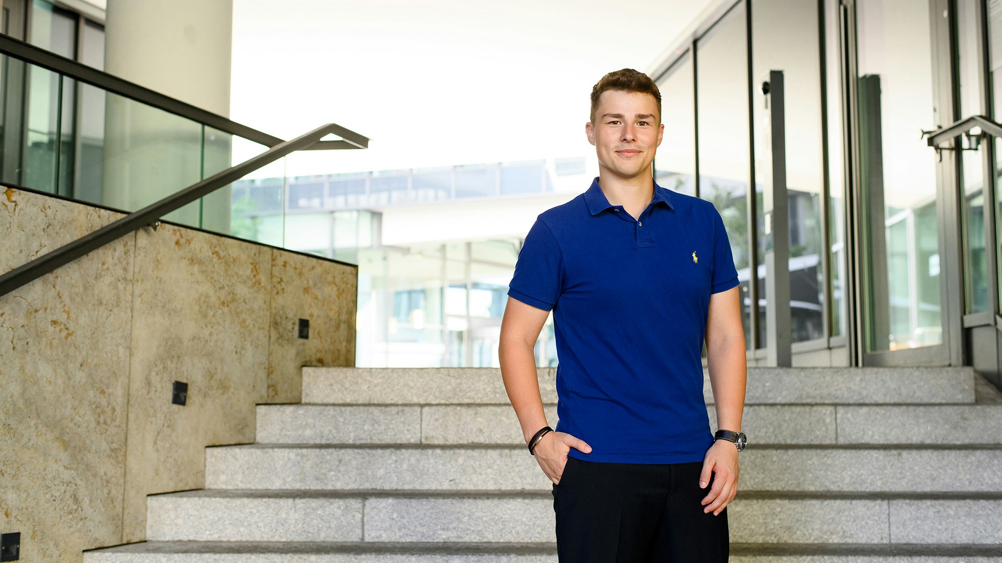 Arne Kupfer in einem blauen Poloshirt, draußen auf einer Treppe eines Bürogebäudes.