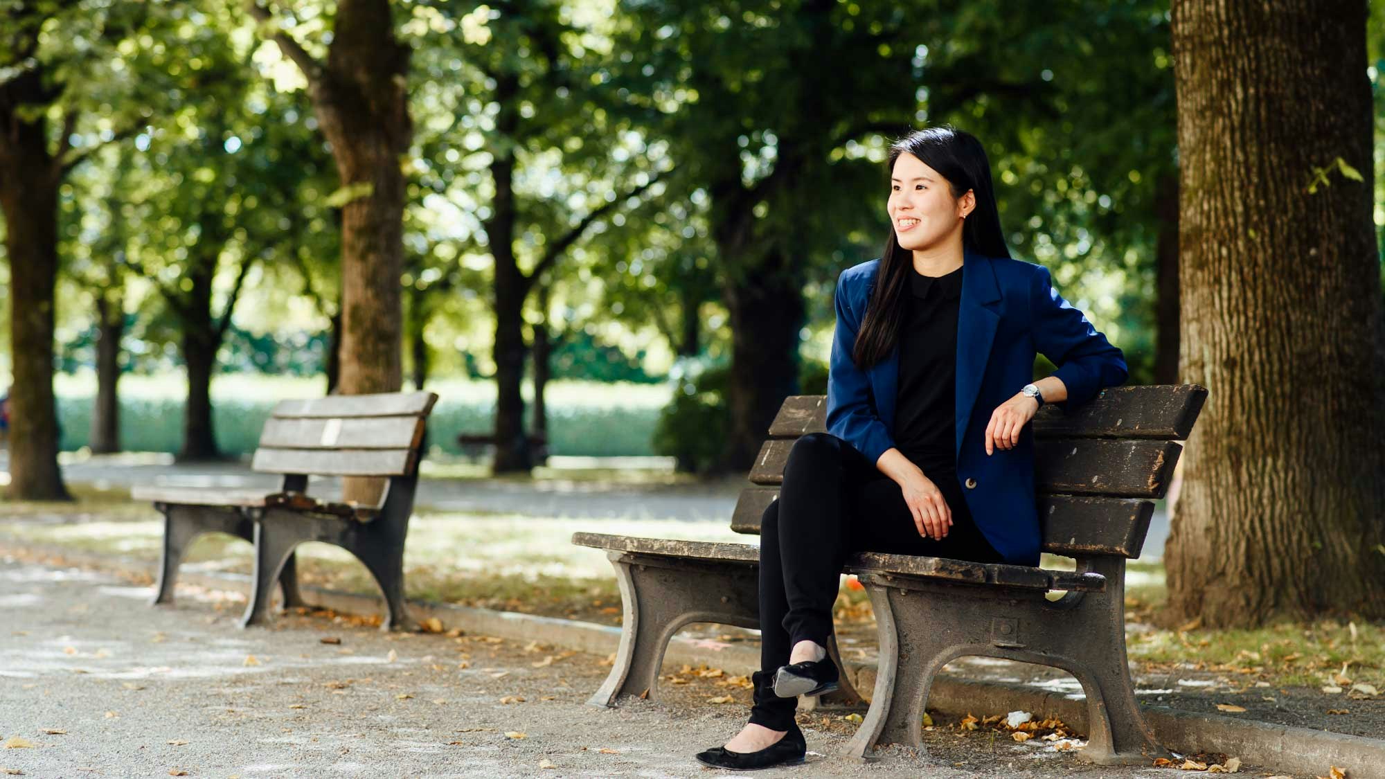 Yi-Chen Liu siting on a park bench smiling, looking away from the camera.