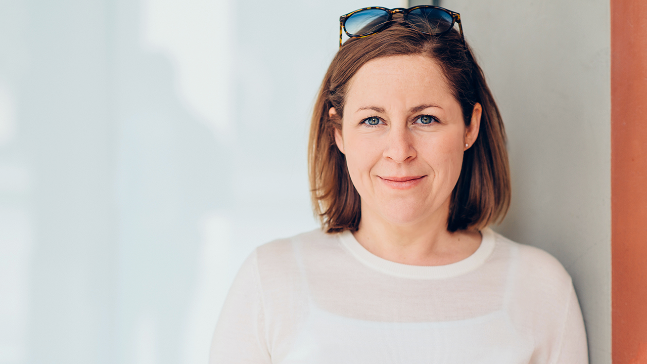 Profile Photo of Sandra Bayer looking directly into the camera, wearing white sweater against bright background.