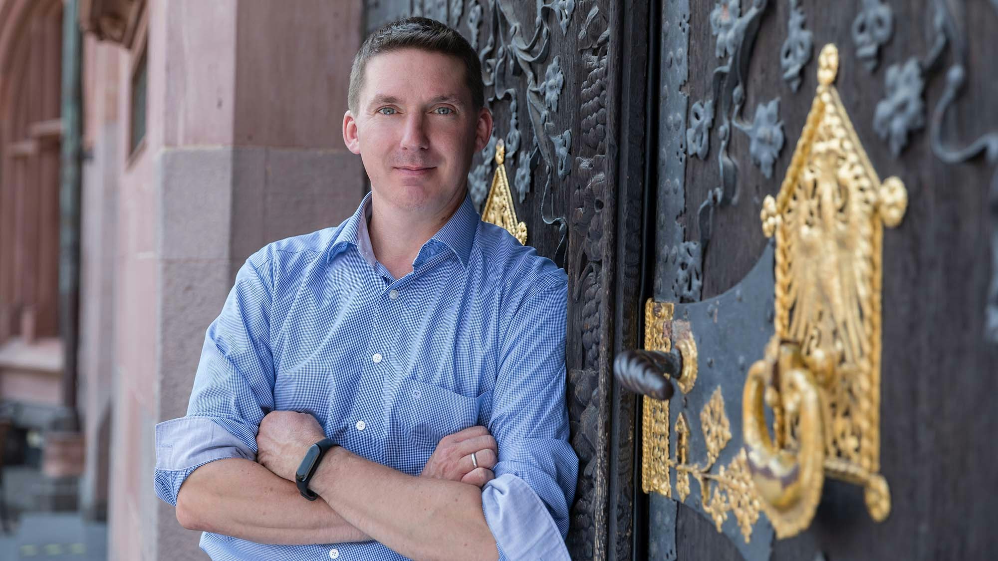 Eric Mueller standing with his arms crossed, leaning against old decorated door.