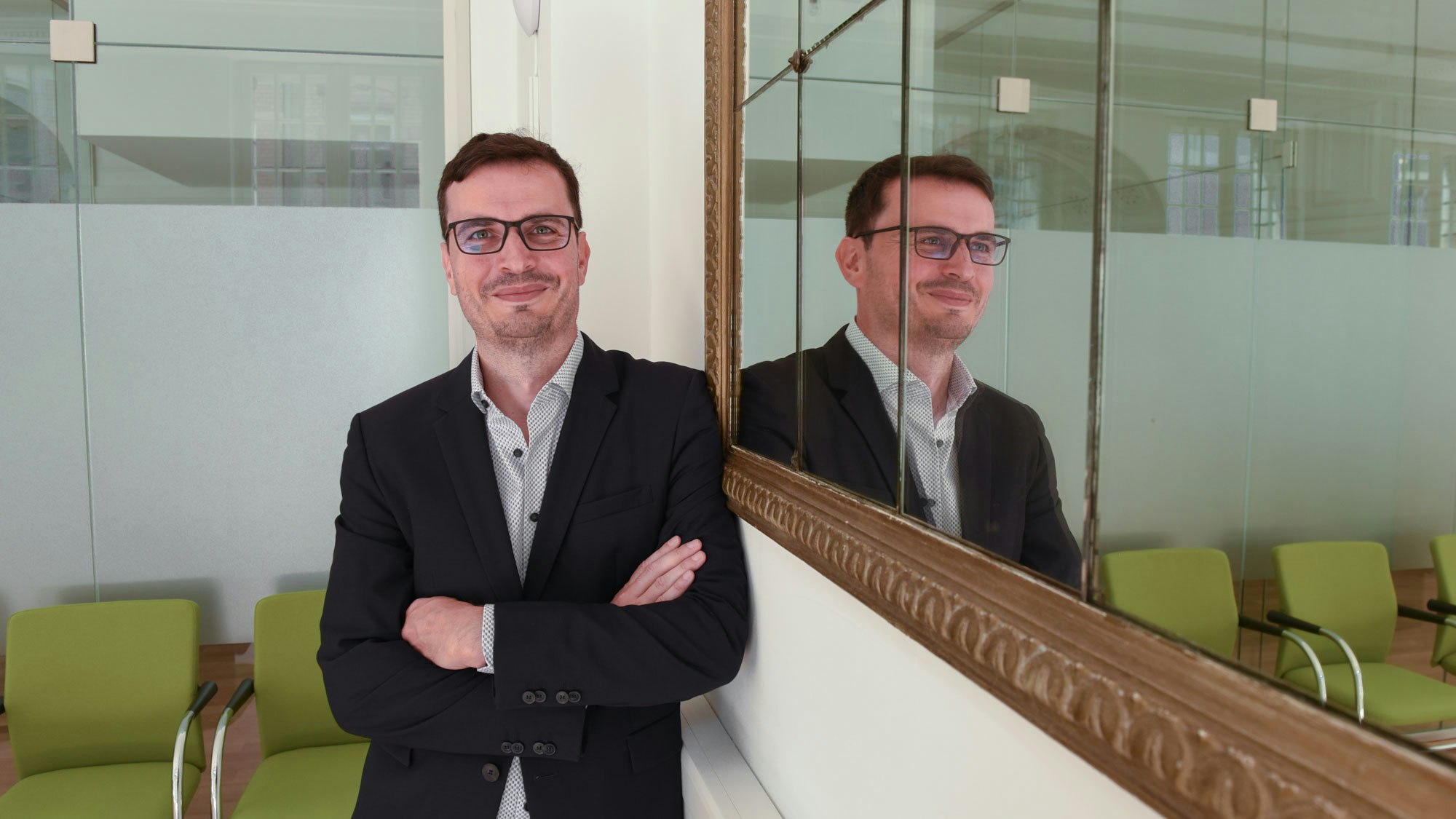 Christian Weih-Sum standing next to a mirror, hands crossed, looking into the camera.