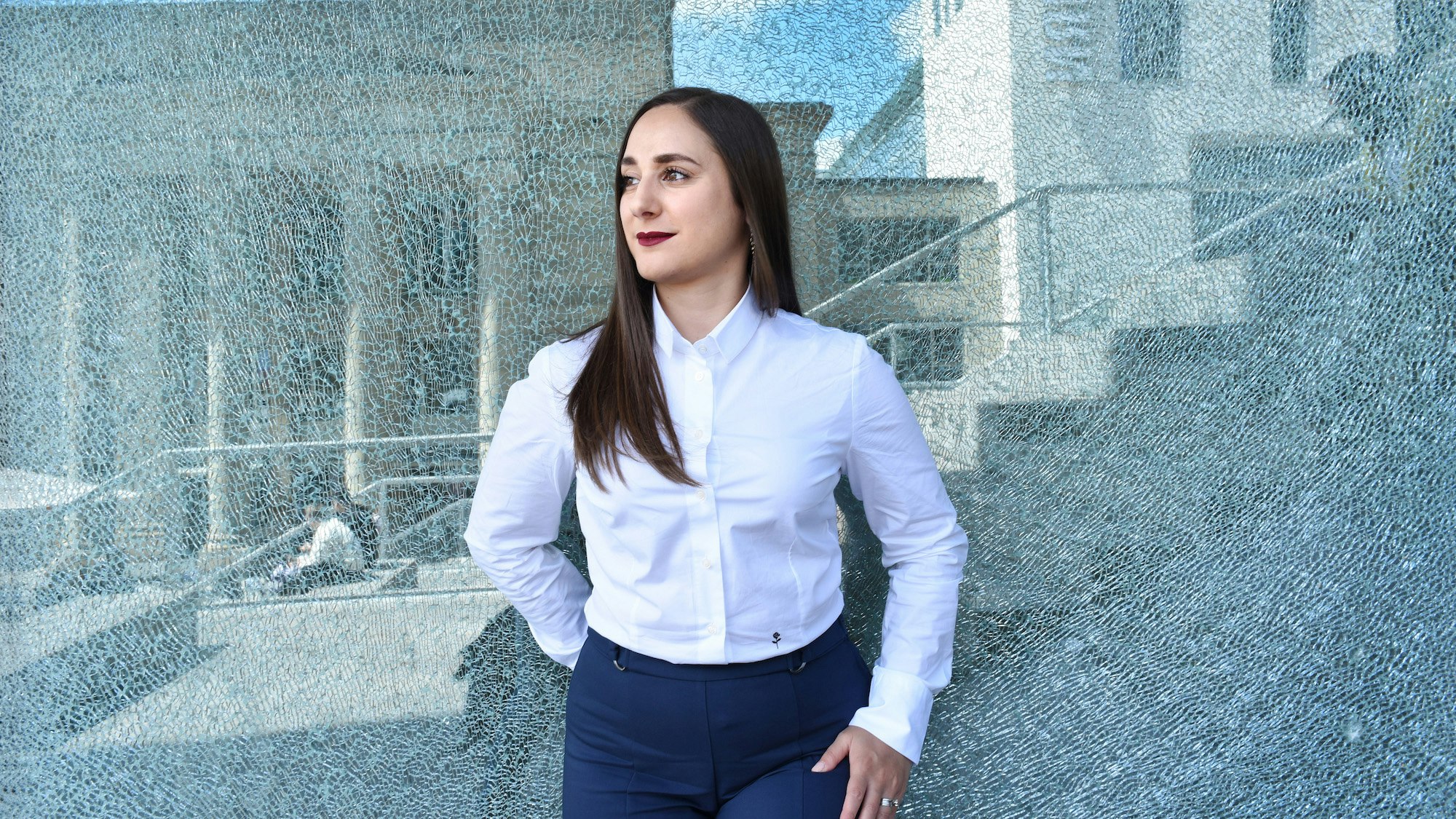 Valentina Zoffreo standing against a glass background, looking to her right, professionally dressed.