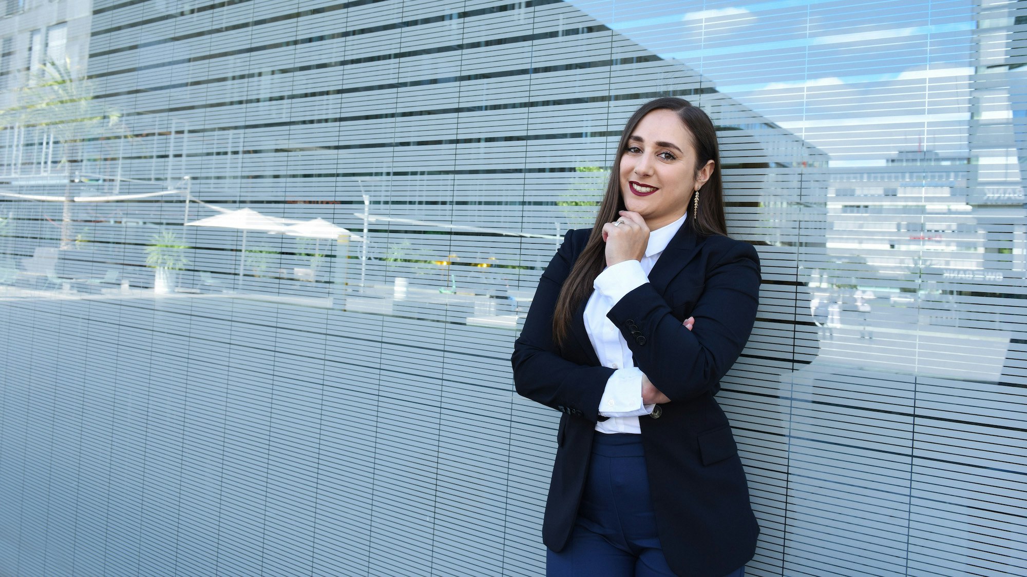 Valentina Zoffreo standing against a glass wall with white stripes, hand under her chin.