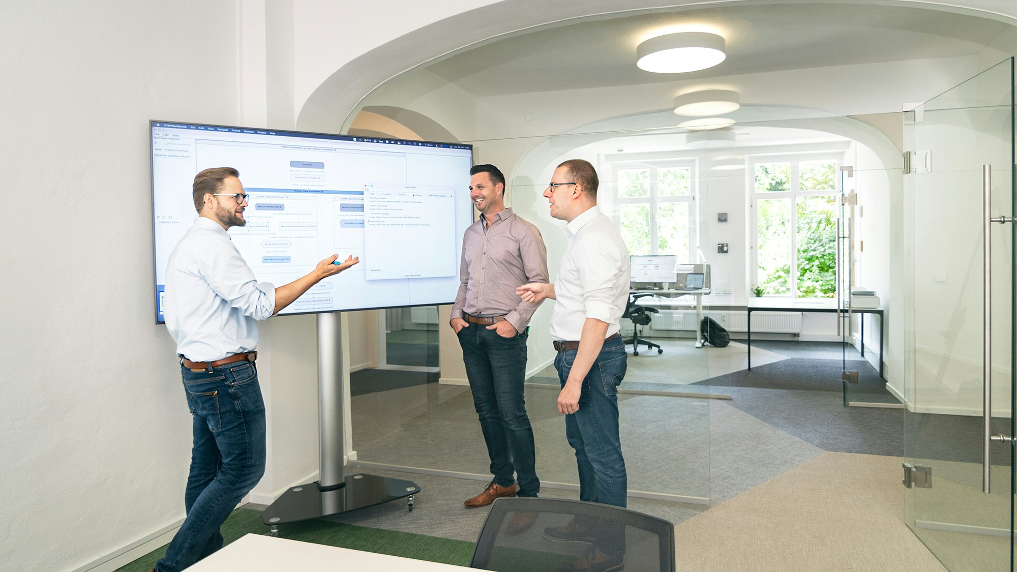 Three people discussing, standing around a large screen in an office setting