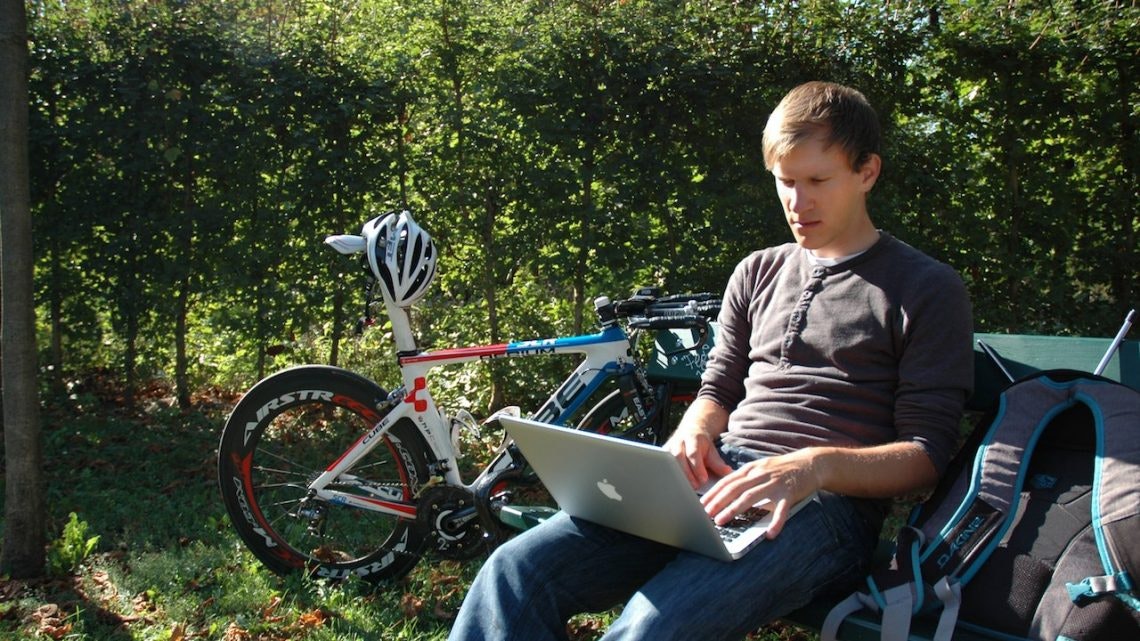 Person, sitting on a bench int he middle of nature browsing their laptop