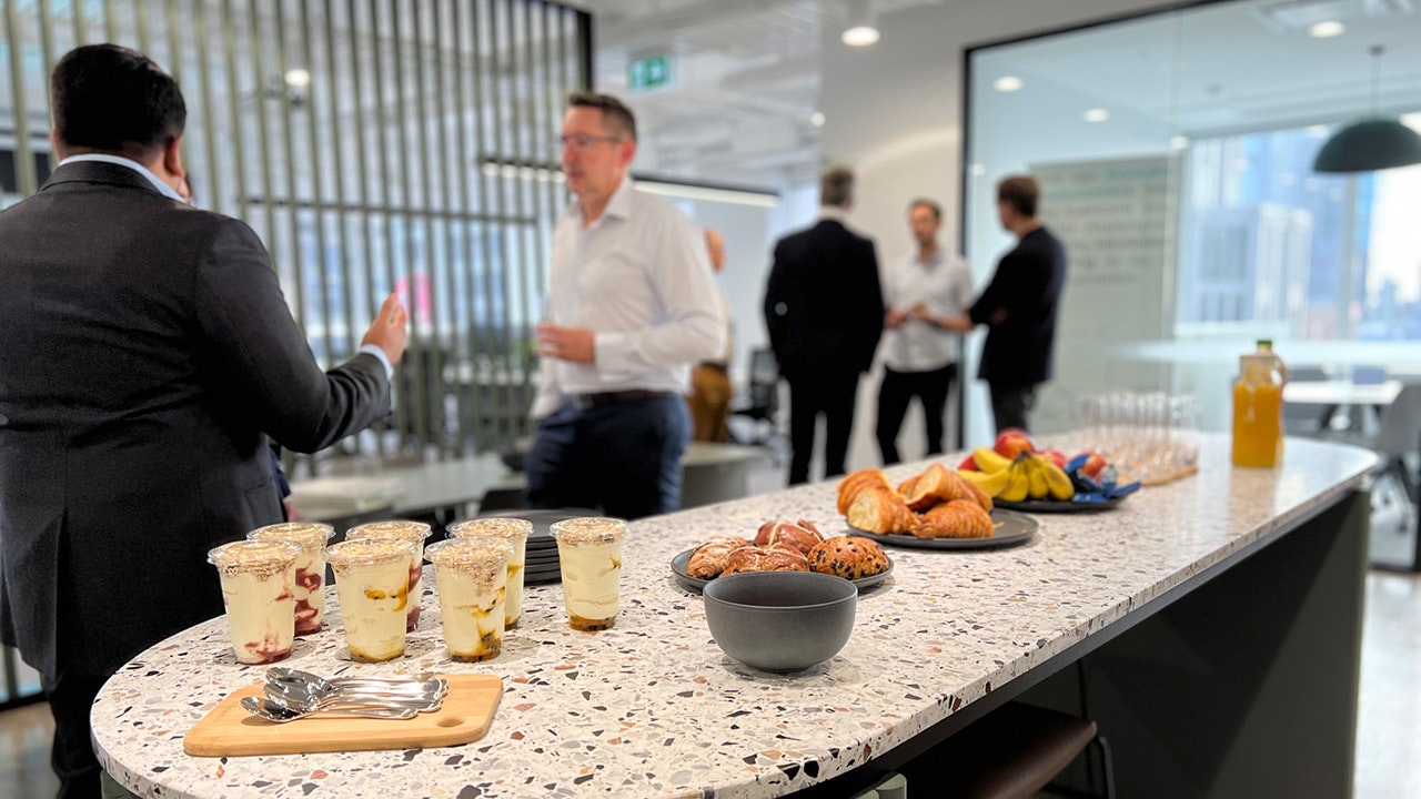 A counter with breakfast buffet and in the background you can see the guests chatting.