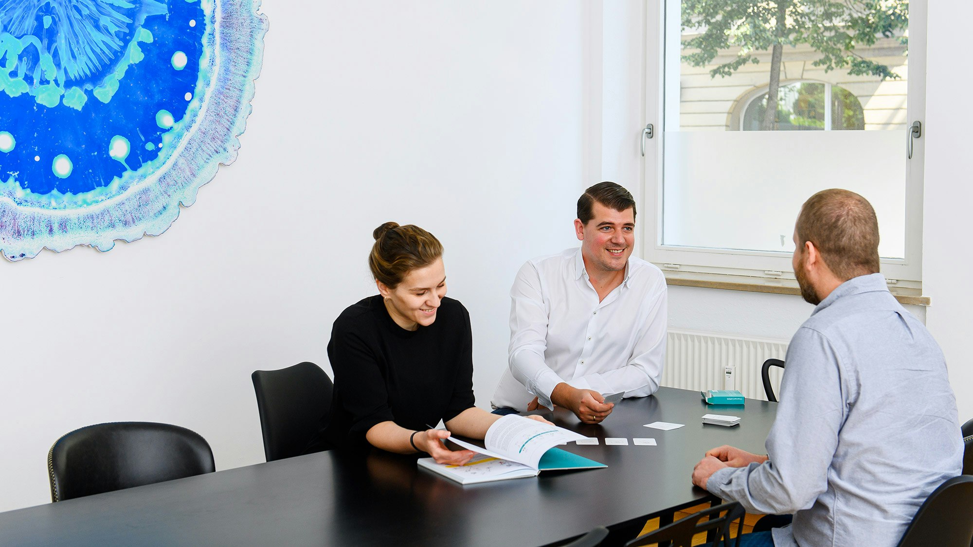 Three colleagues sit at the black meeting table and deal with ChannelOPERA from foryouandyourcustomers.