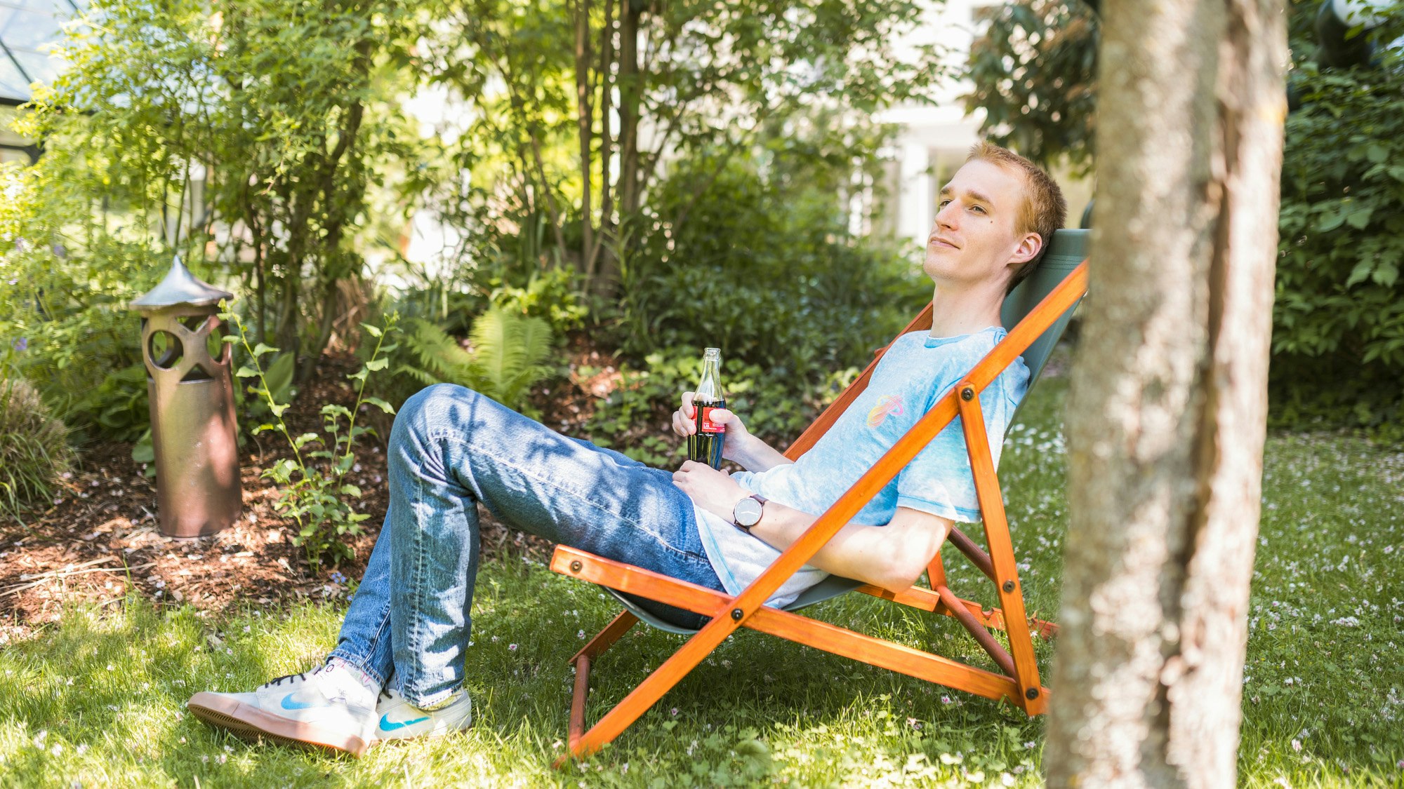 Martin Smazil relaxing in a garden folding chair, with a bottle of Cola in his hand.