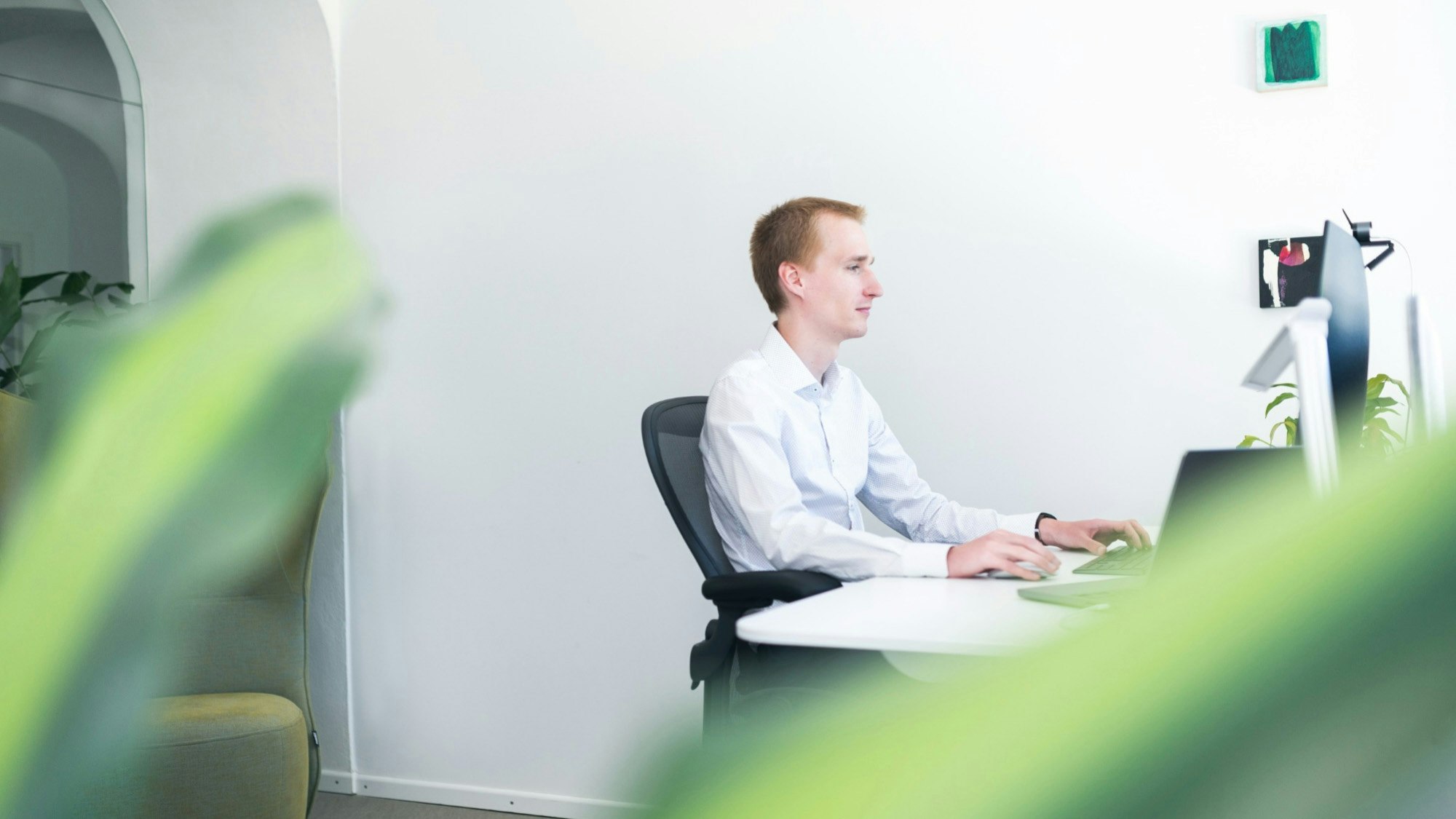 Martin Smazil aus der Ferne, an seinem Laptop arbeitend, mit unscharfen Pflanzenblättern im Vordergrund.