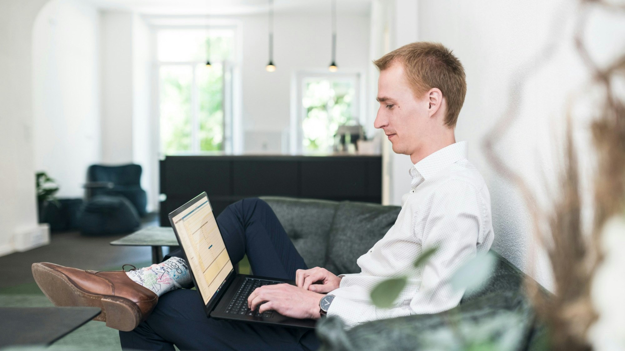 Martin Smazil sitzt auf einem Sofa in einem schönen modernen Büro und arbeitet an seinem Laptop.