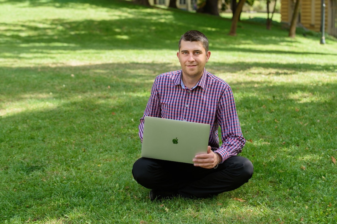 Nikolay sitting in a field of grass with a laptop on his lap