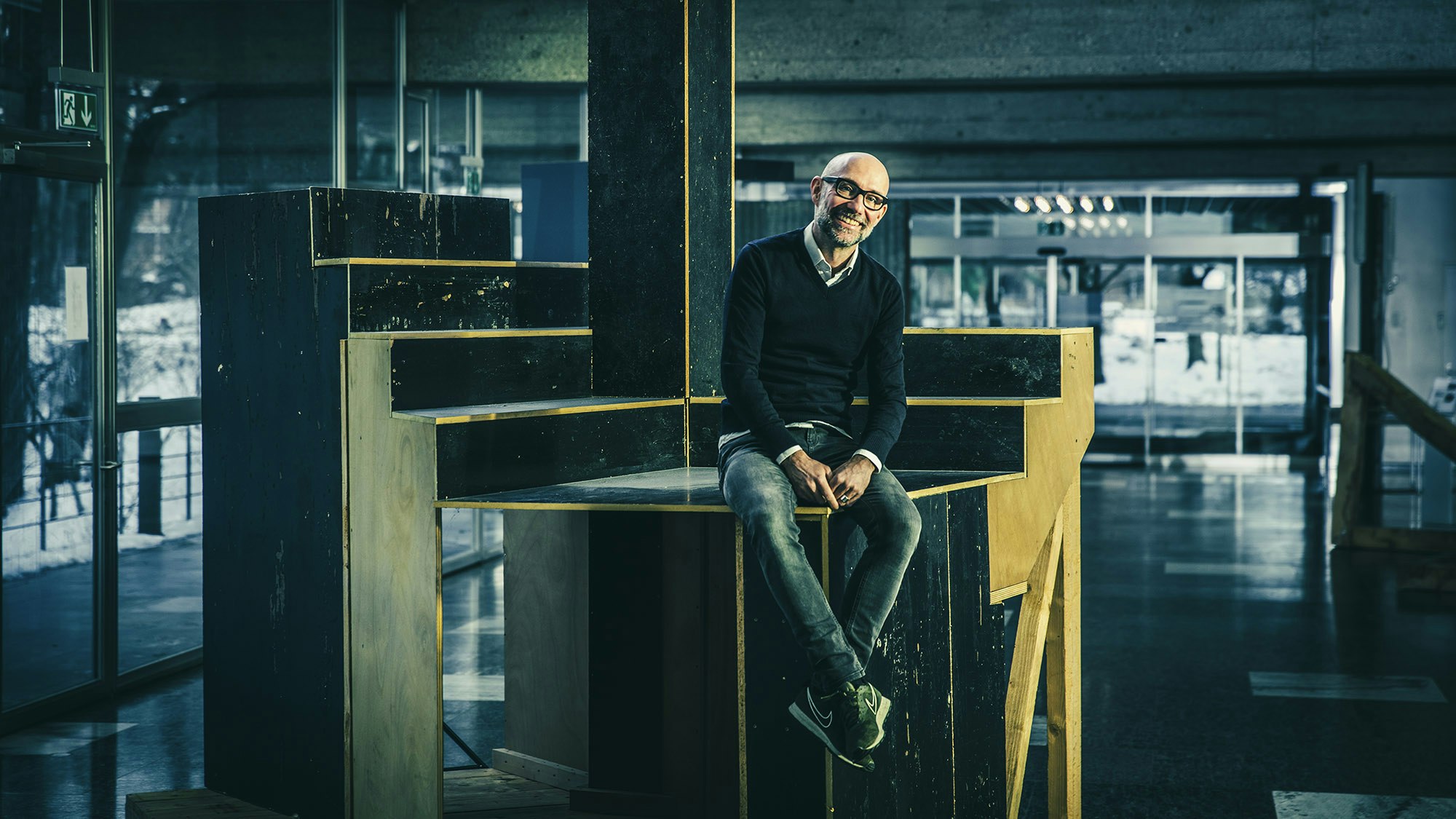 Man sitting on a artwork made of wood in the form of stairs.