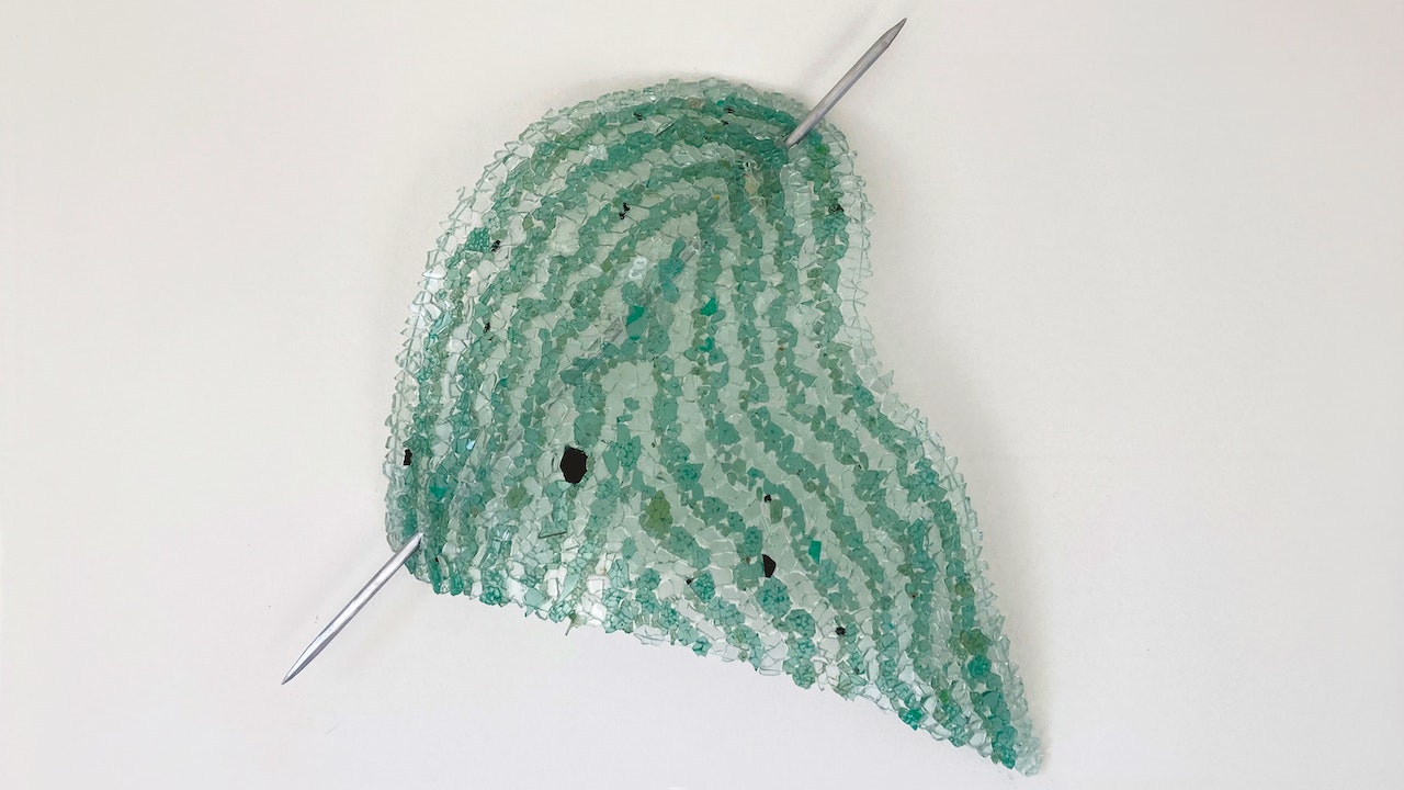 Driedimensionaal kunstwerk, groenblauwe vorm doorstoken van een grote naald.