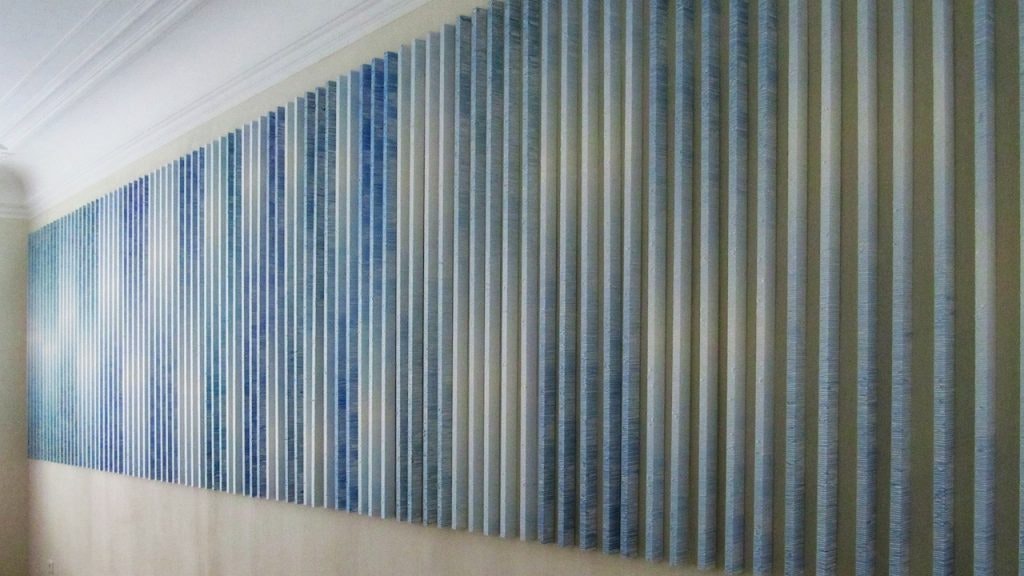 Verschillende tinten blauwe plankachtige kunstwerken die de hele muur vullen.