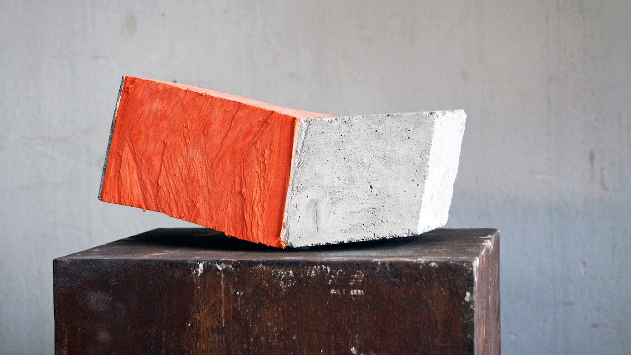 A sculpture standing on a wooden pillar, a block of two colours. , The left side of the object is orange, right part of the object white.