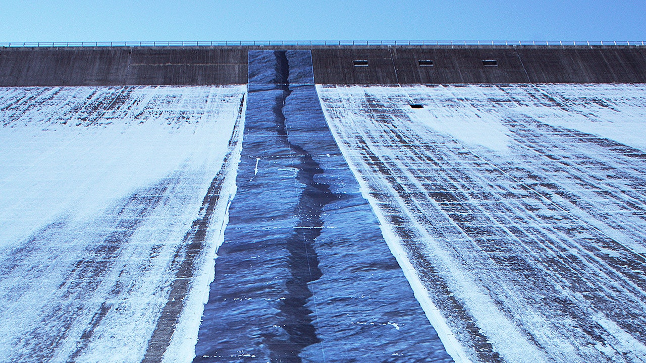Ein Foto einer mit Schnee bedeckten Staumauer, die durch einen kunstvoll eingefügten Riss vertikal gespalten ist.
