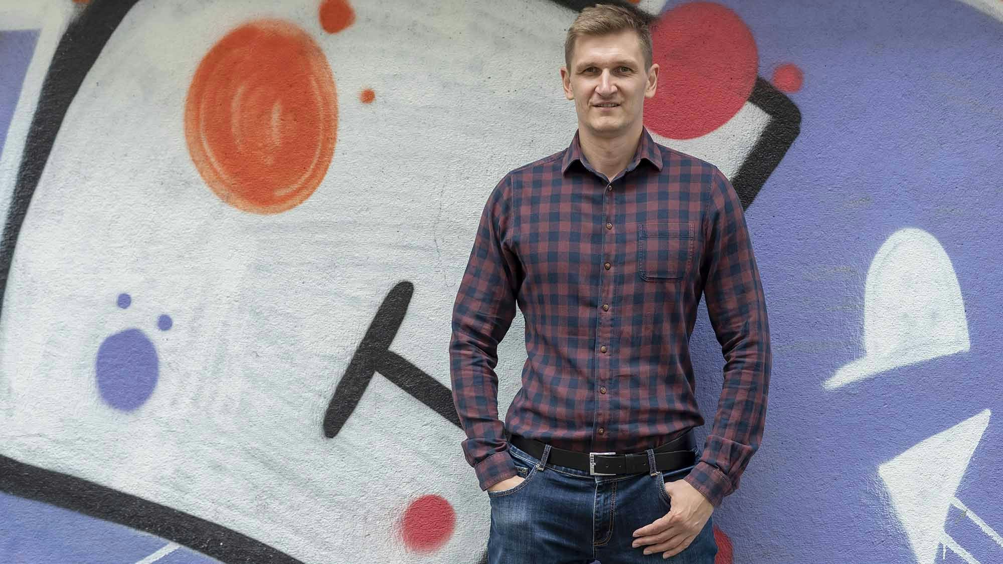 Young man in a checkered shirt standing in front of a graffiti sprayed wall.