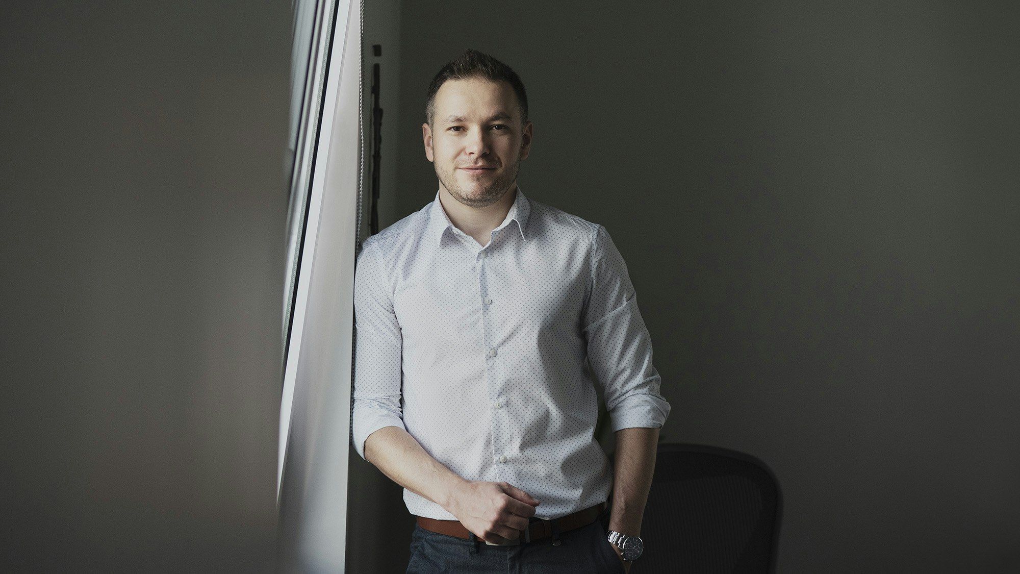 Young man in business surroundings standing by the window.