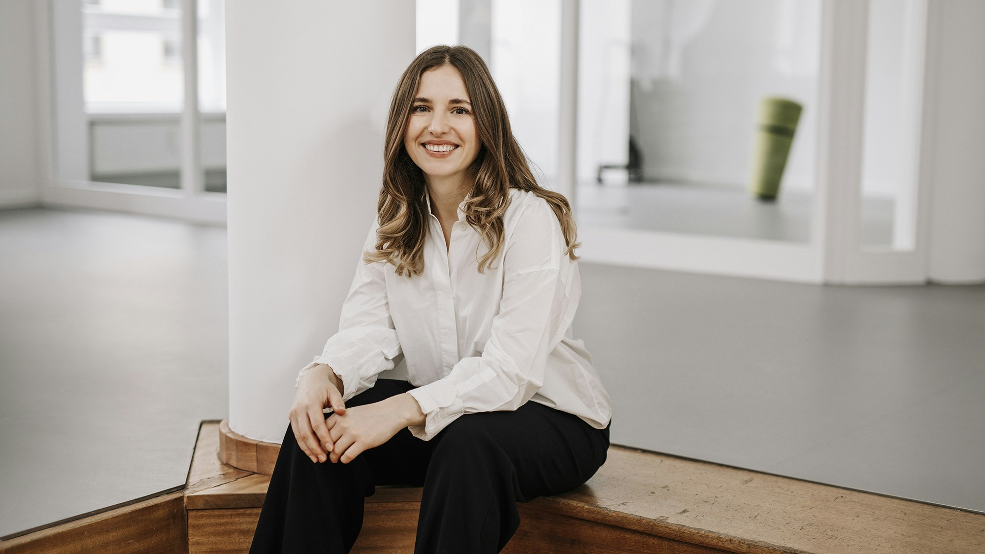 Anna Stark sitzt auf einer Stufe im Frankfurter Büro und lächelt in die Kamera
