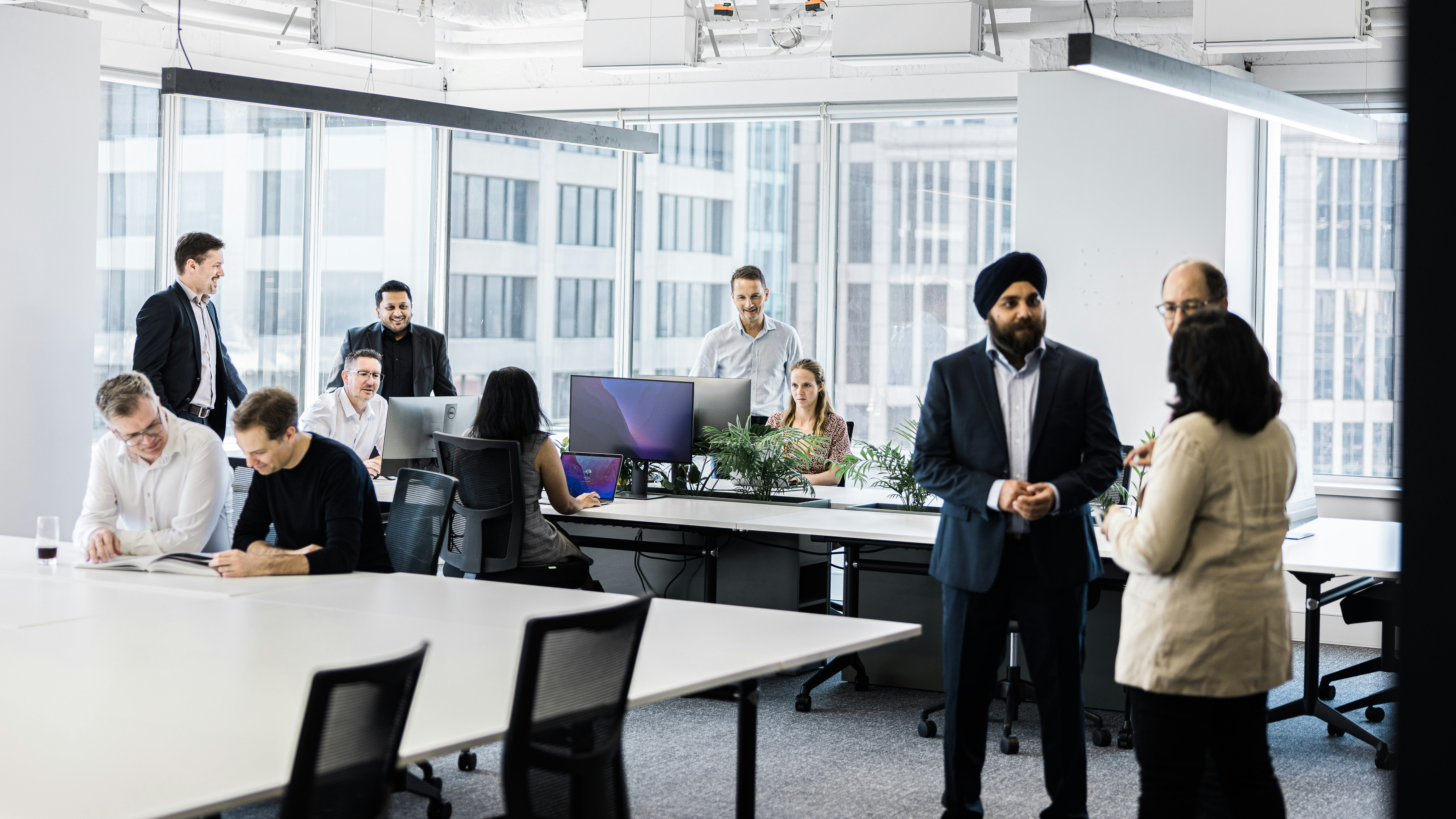 People interact in small groups in a modern office with glass walls.
