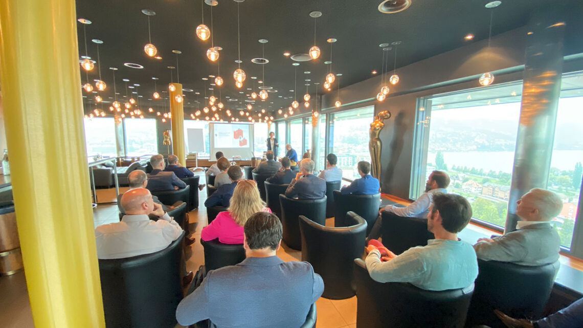 A conference room filled with people sitting in leather seats, you see their backs as they are watching a presentation.