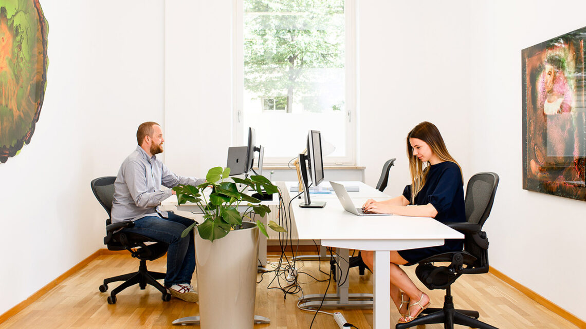 Eine junge Frau und ein Mann arbeiten in einem mit Kunstwerken dekorierten Büro.