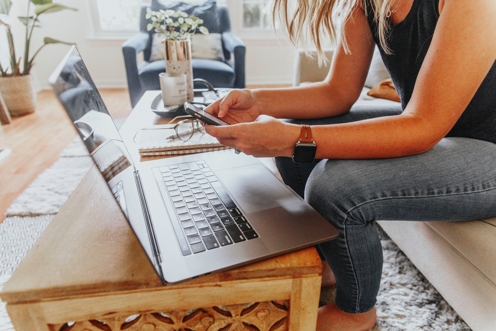 A woman on a couch with a laptop and a smartphone in her hands.