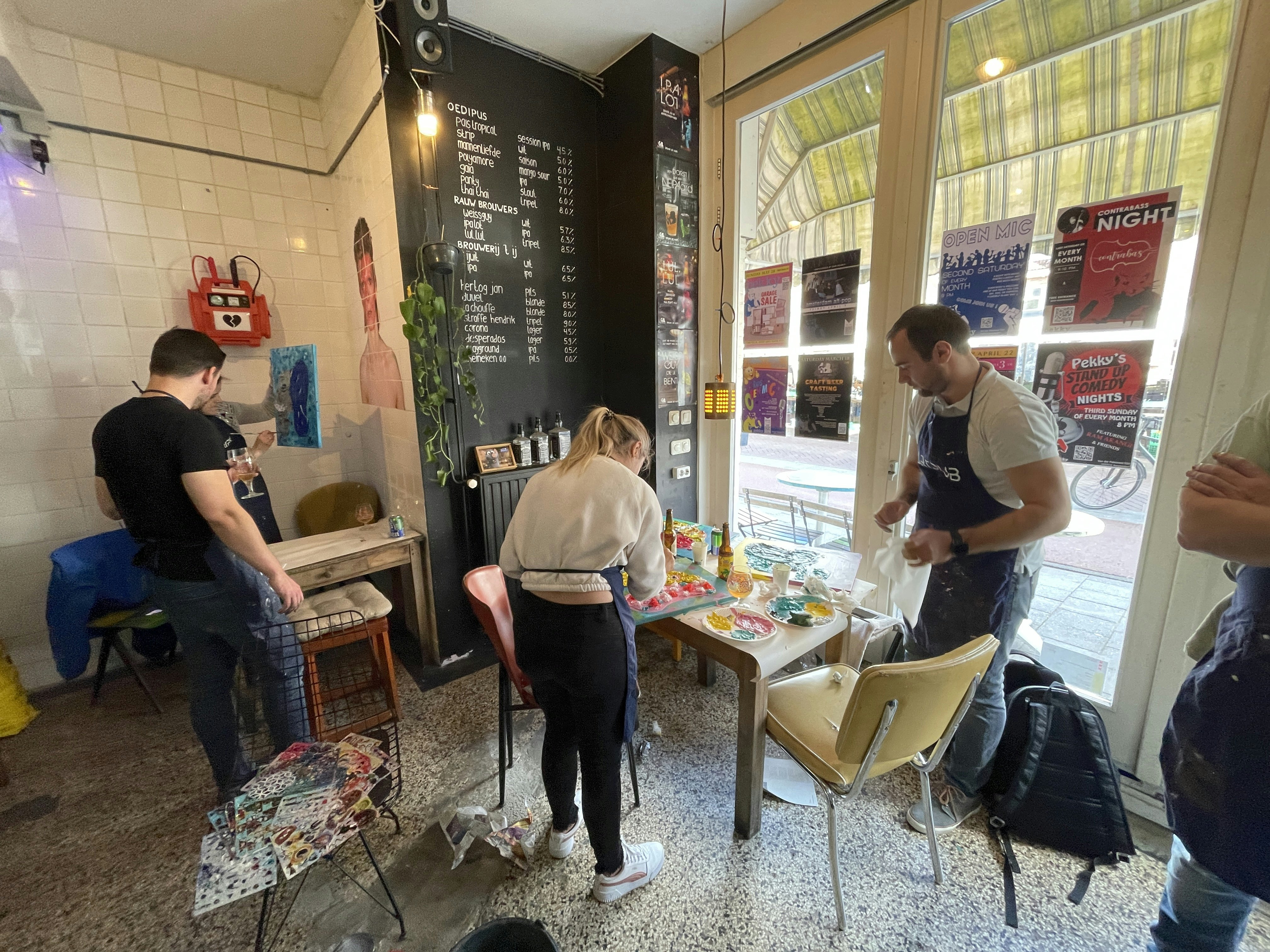 People with aprons working on their art pieces in a bar with art supplies on the floor around them.