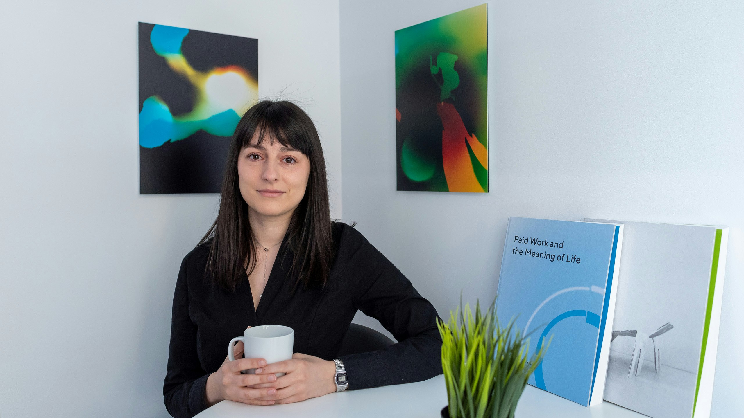 A young woman holding coffee next to hanged art.