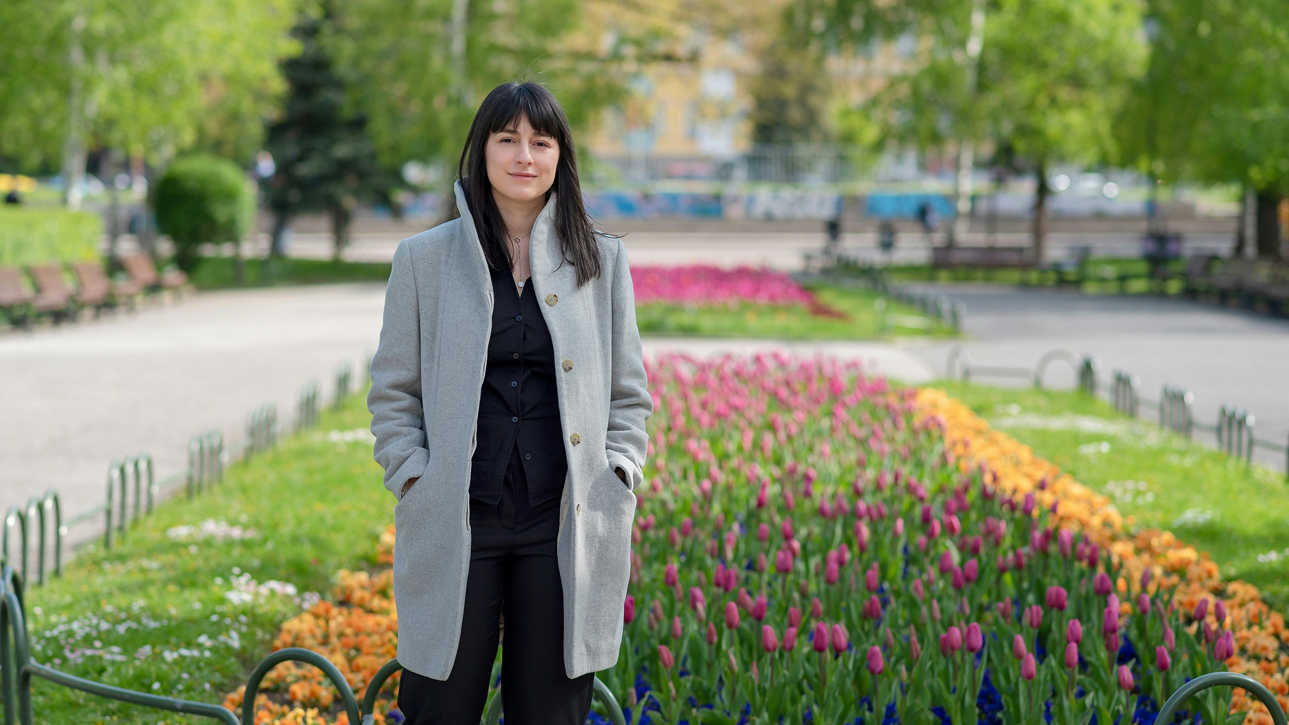 A young woman in front of flower-bed.