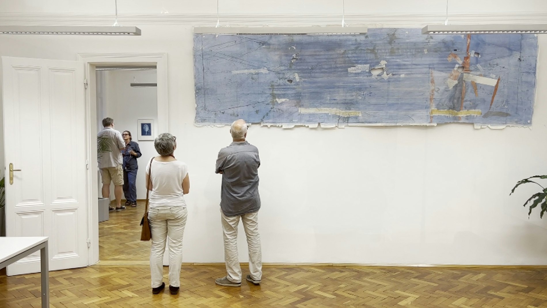 Zwei Personen betrachten ein blaues Kunstwerk, das an einer Wand in einem Büro hängt.