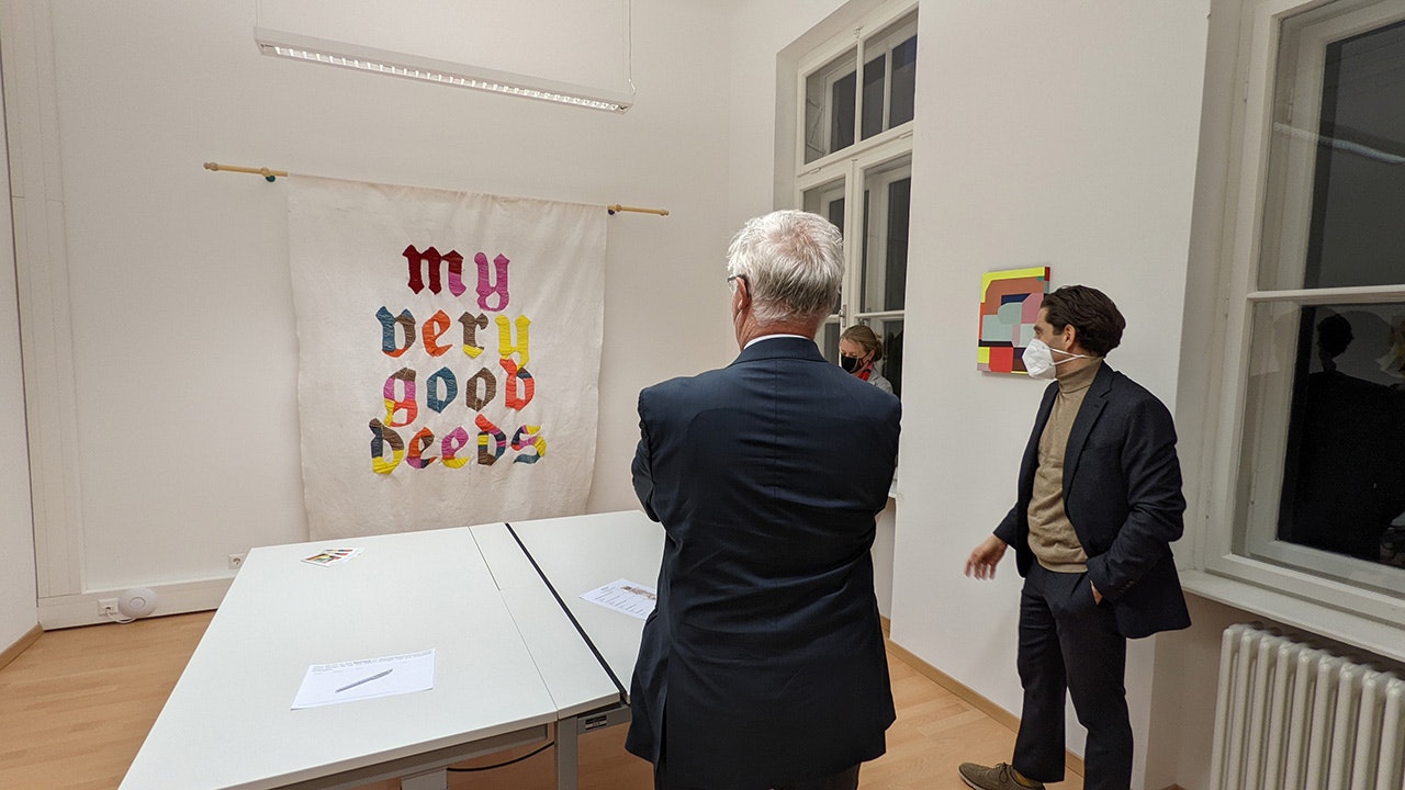 Zwei Männer in einem Büroraum betrachten ein an der Wand hängendes Transparent.