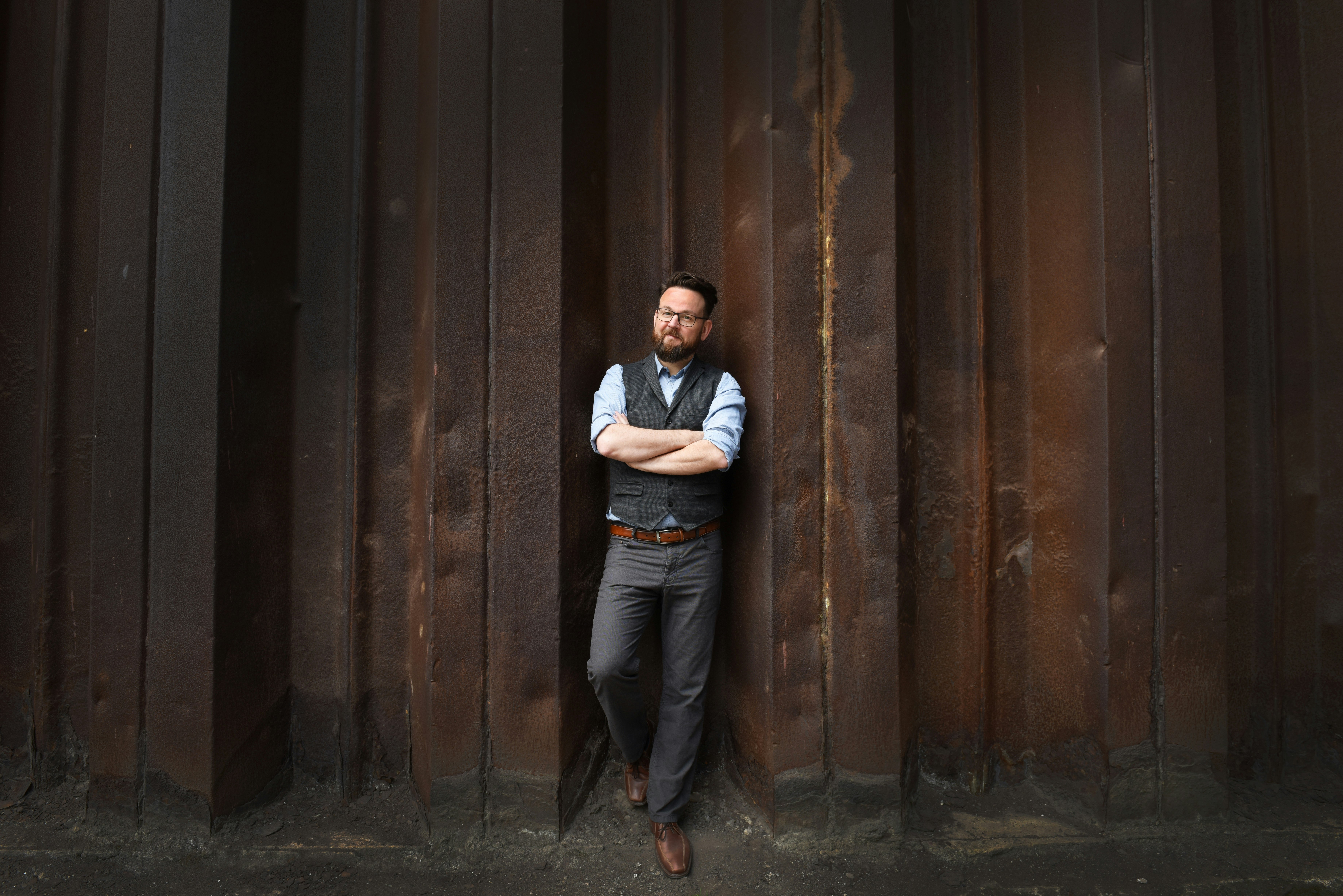 Person wearing a vest standing in front of a rusty wall