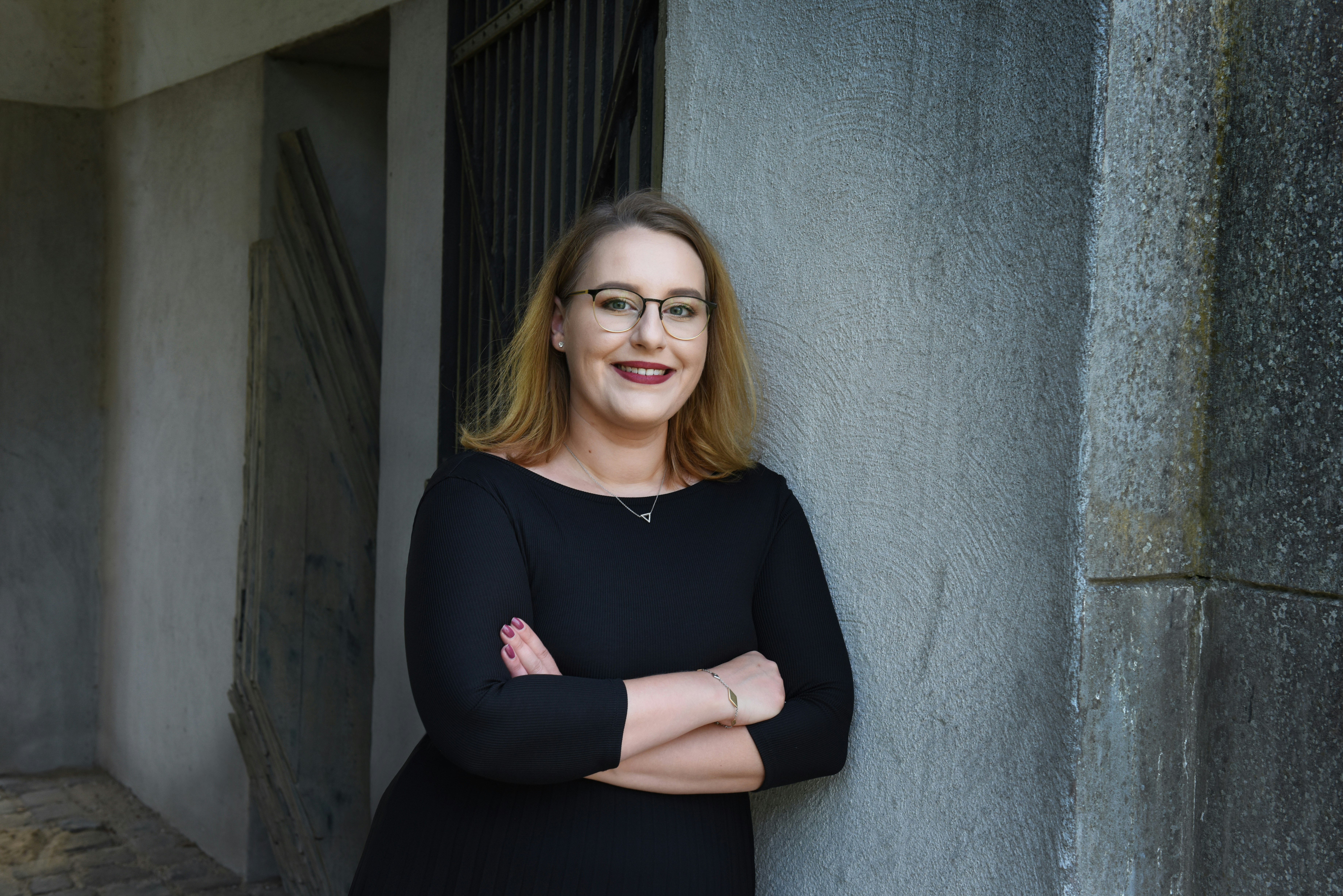 Person wearing glasses standing on a corner with arms crossed