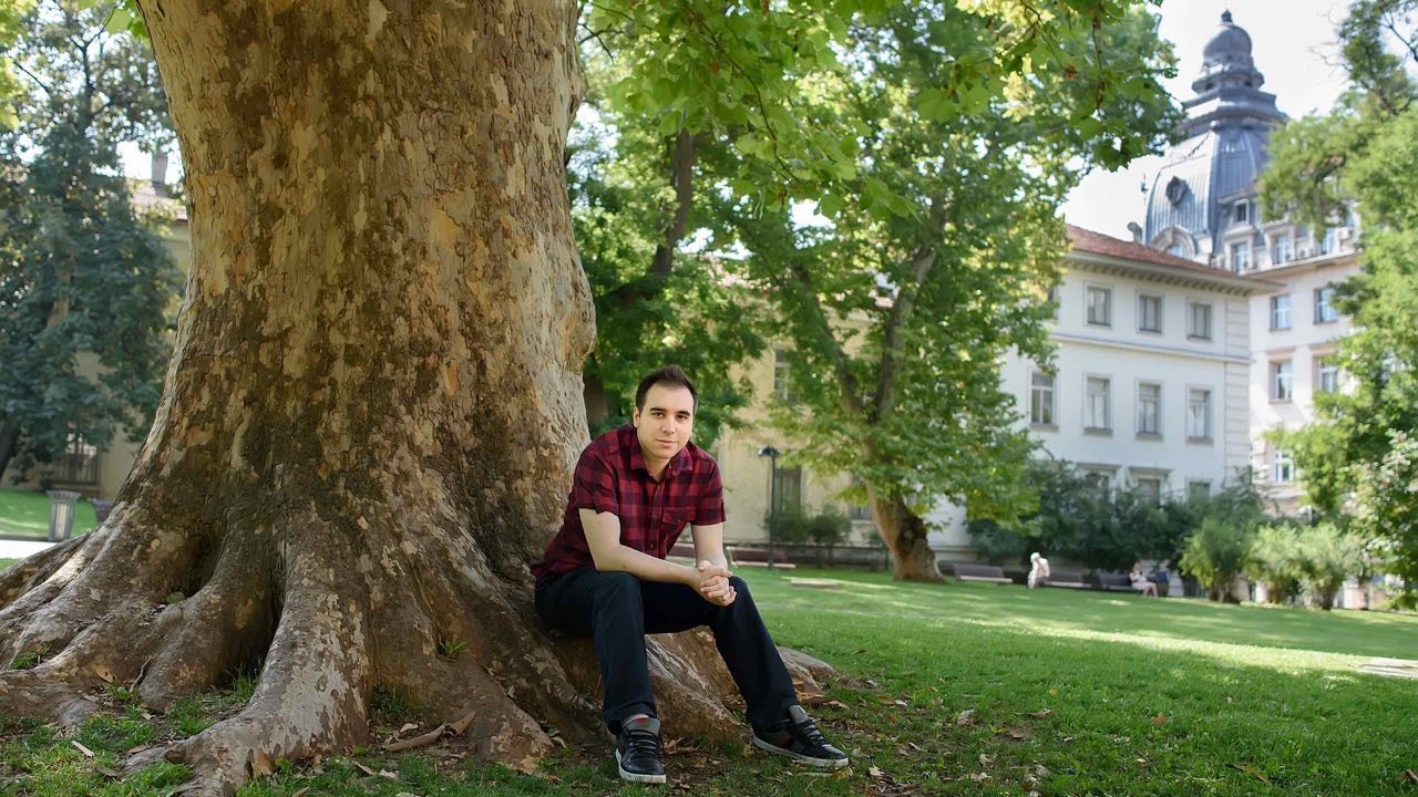 Junger Mann steht neben einem Baum.