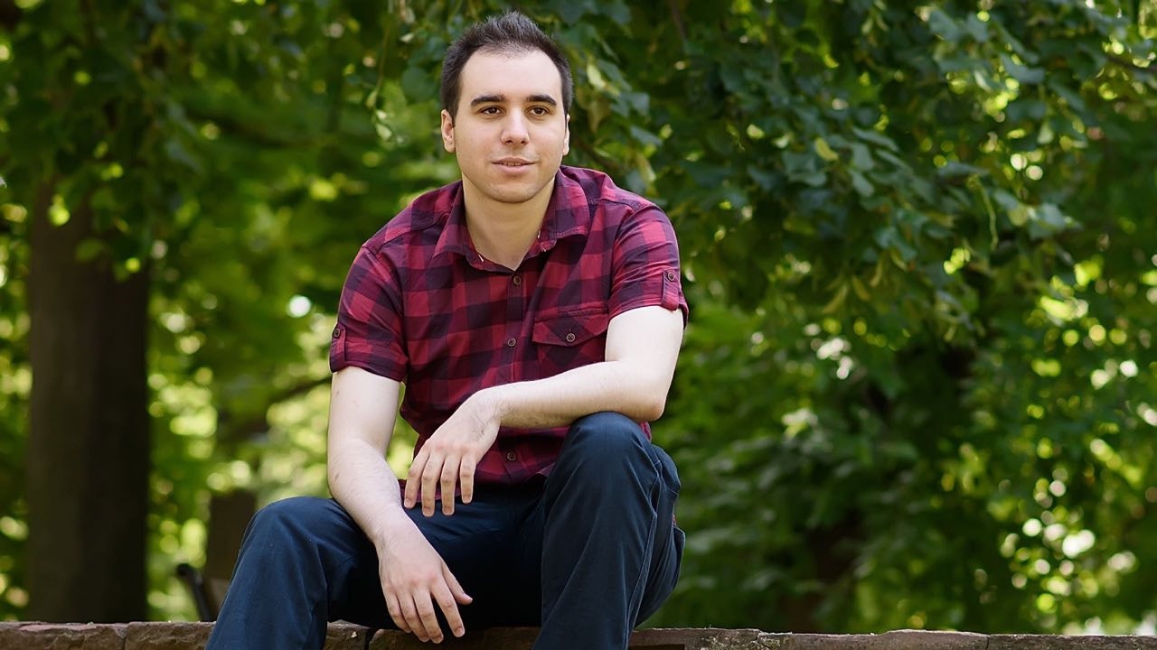 Young man standing in front of tree area.