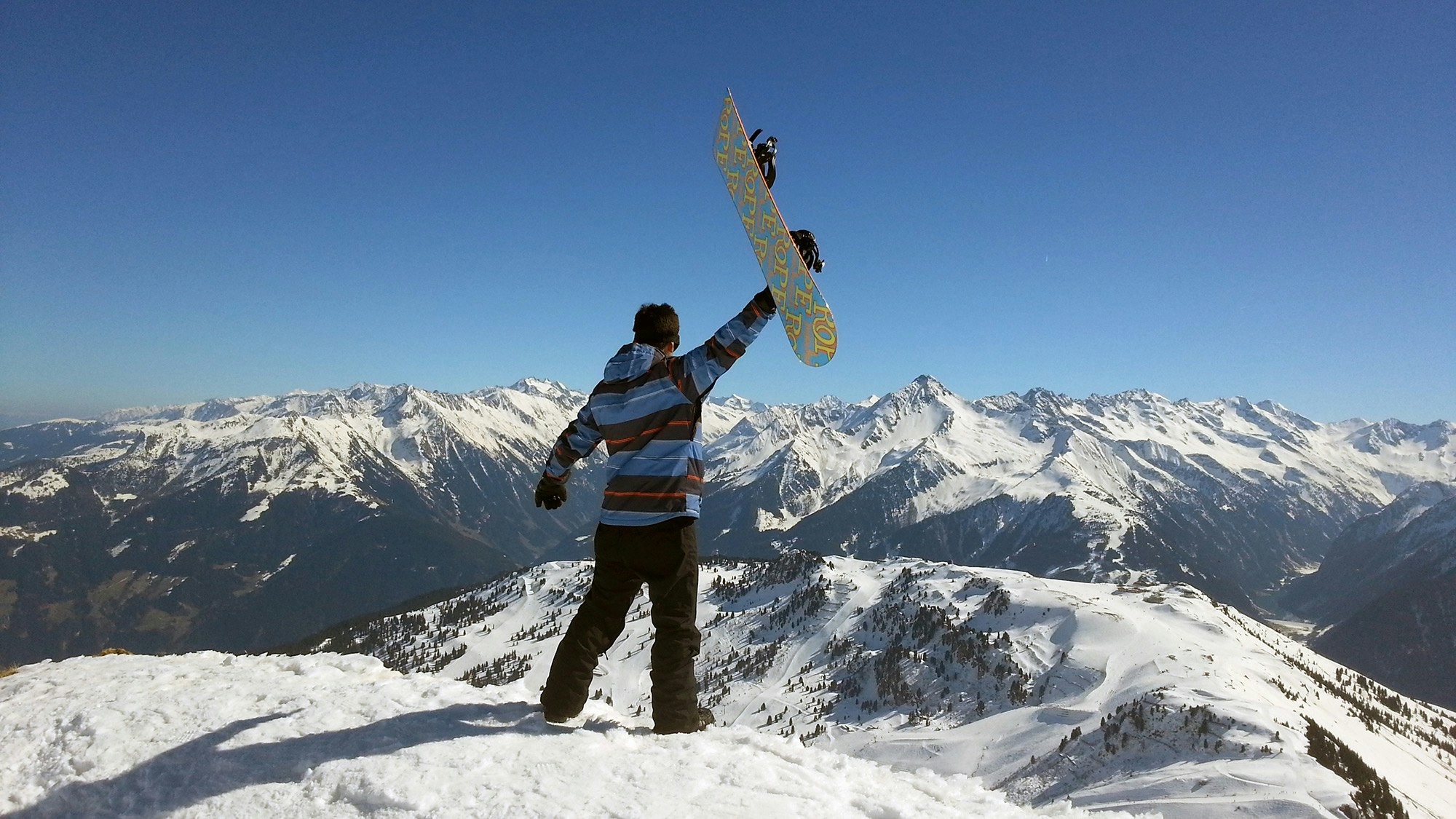 Mann mit Snowboard auf einem Berggipfel.