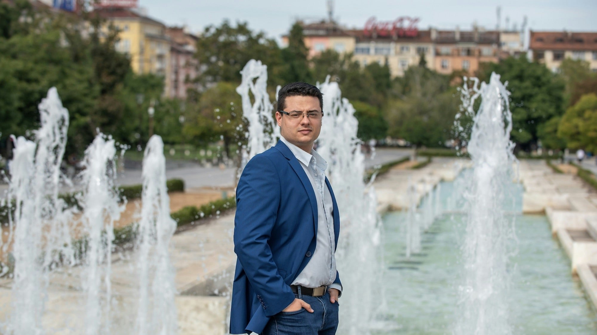 Junger Mann steht vor einem Wasserbrunnen im Stadtgebiet.