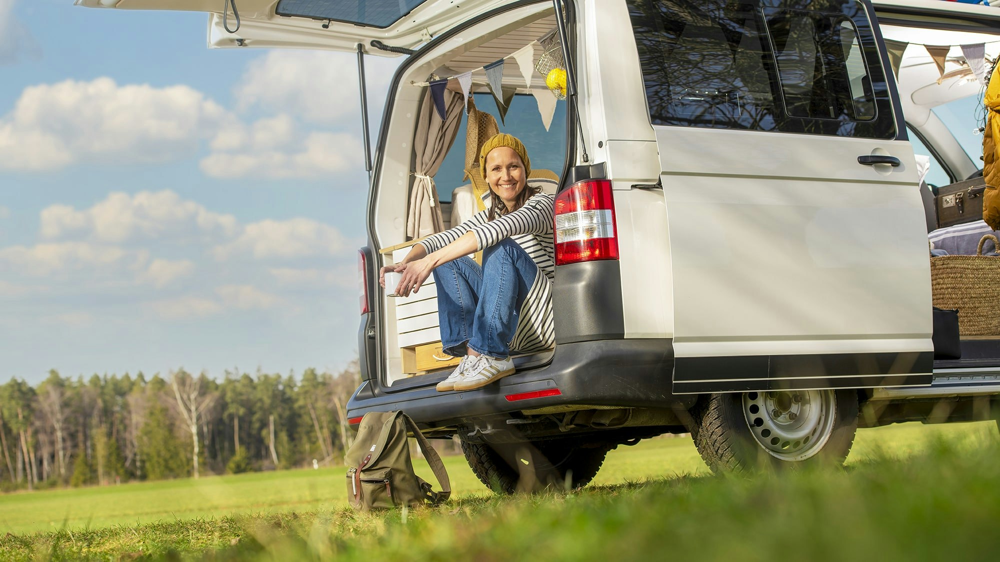 Frau mit Wollmütze sitzt in offenem Camper.