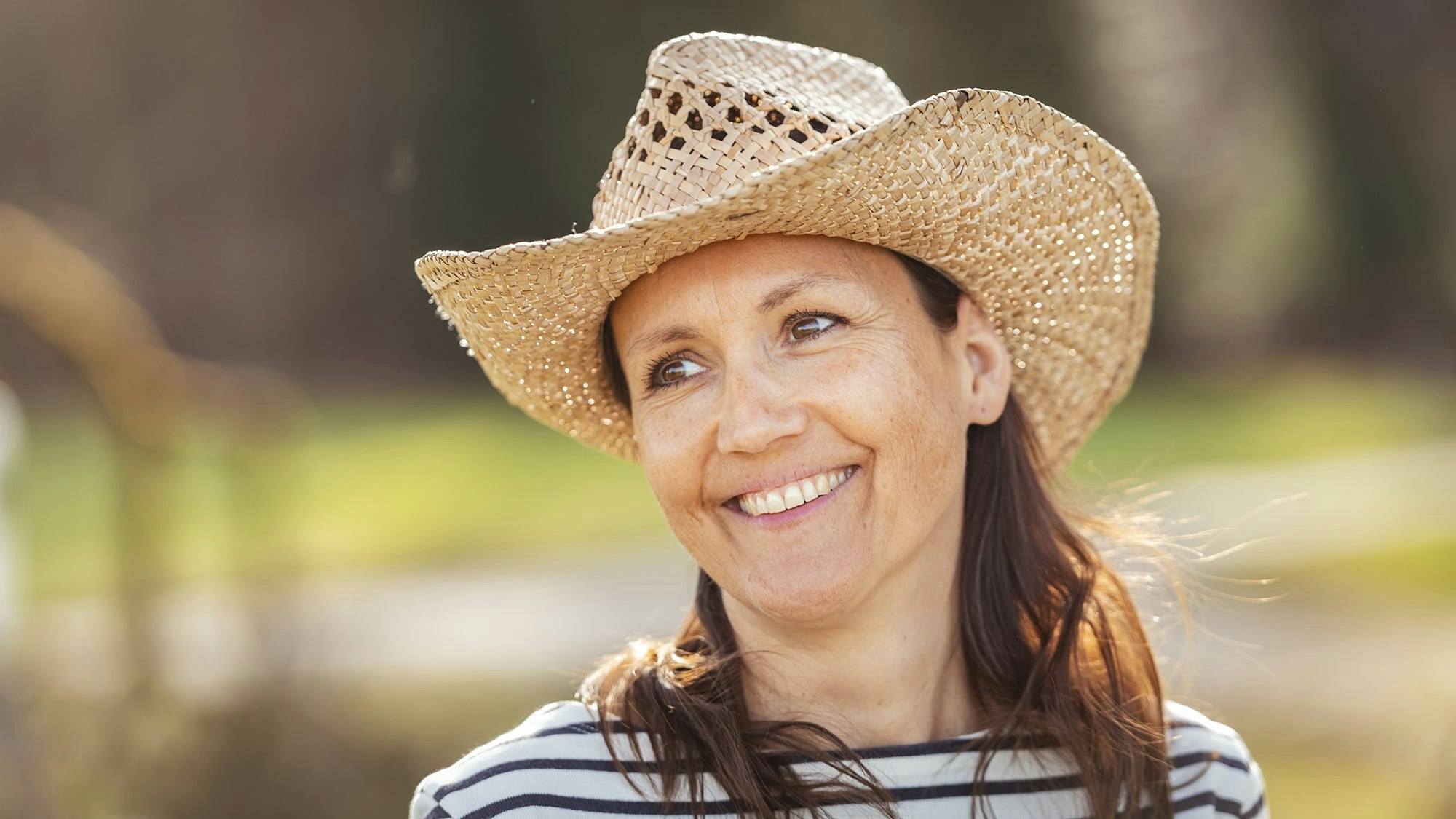 Woman with straw hat and navy shirt outside in nature