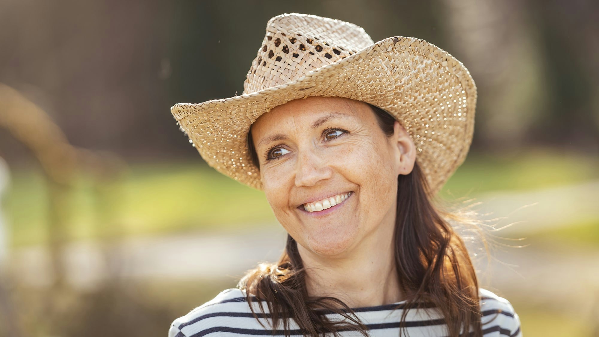Frau mit Strohhut in Streifenshirt draussen in der Natur.