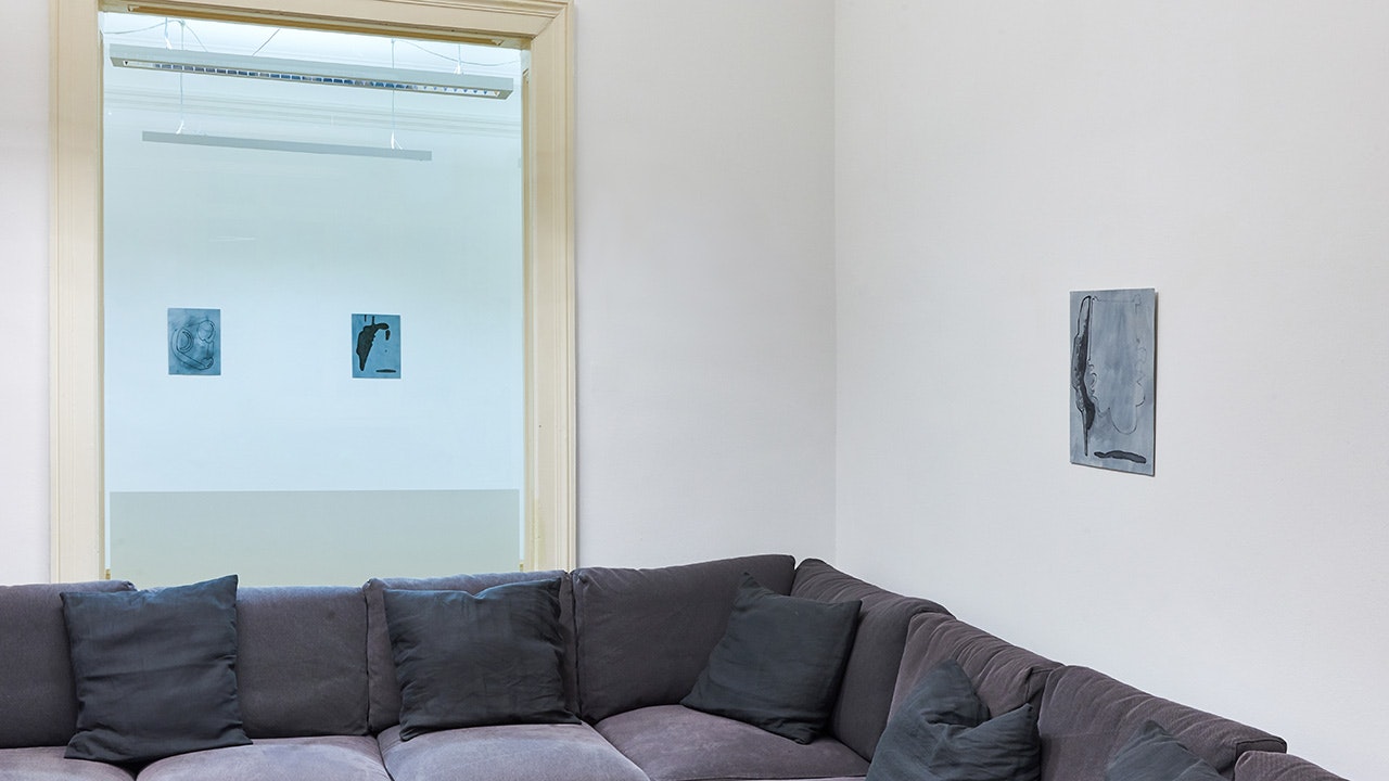 Grau-Blaue kleinformatige Werke hängen an den Wänden, ebenso ist eine graue große Couch zu sehen.