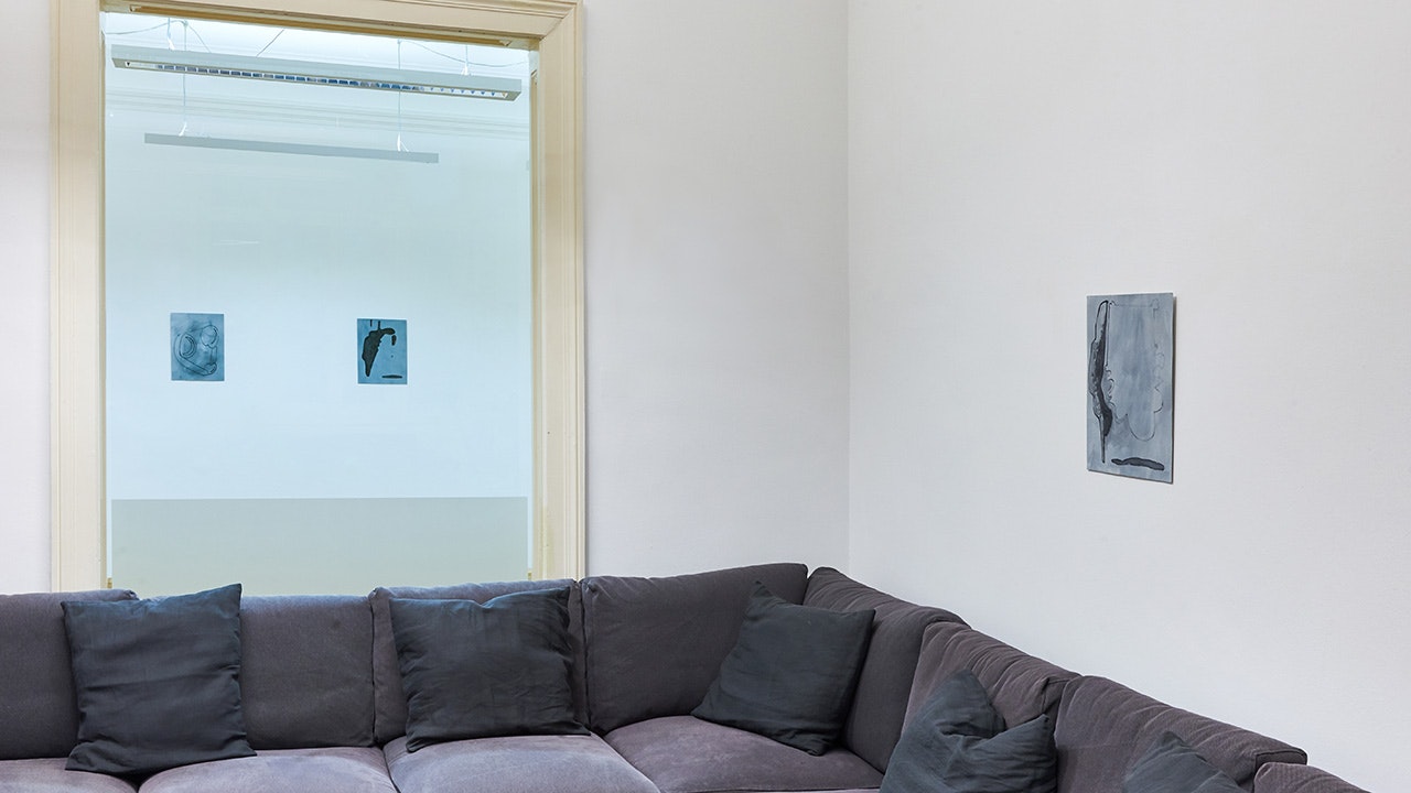 Grau-Blaue kleinformatige Werke hängen an den Wänden, ebenso ist eine graue große Couch zu sehen.