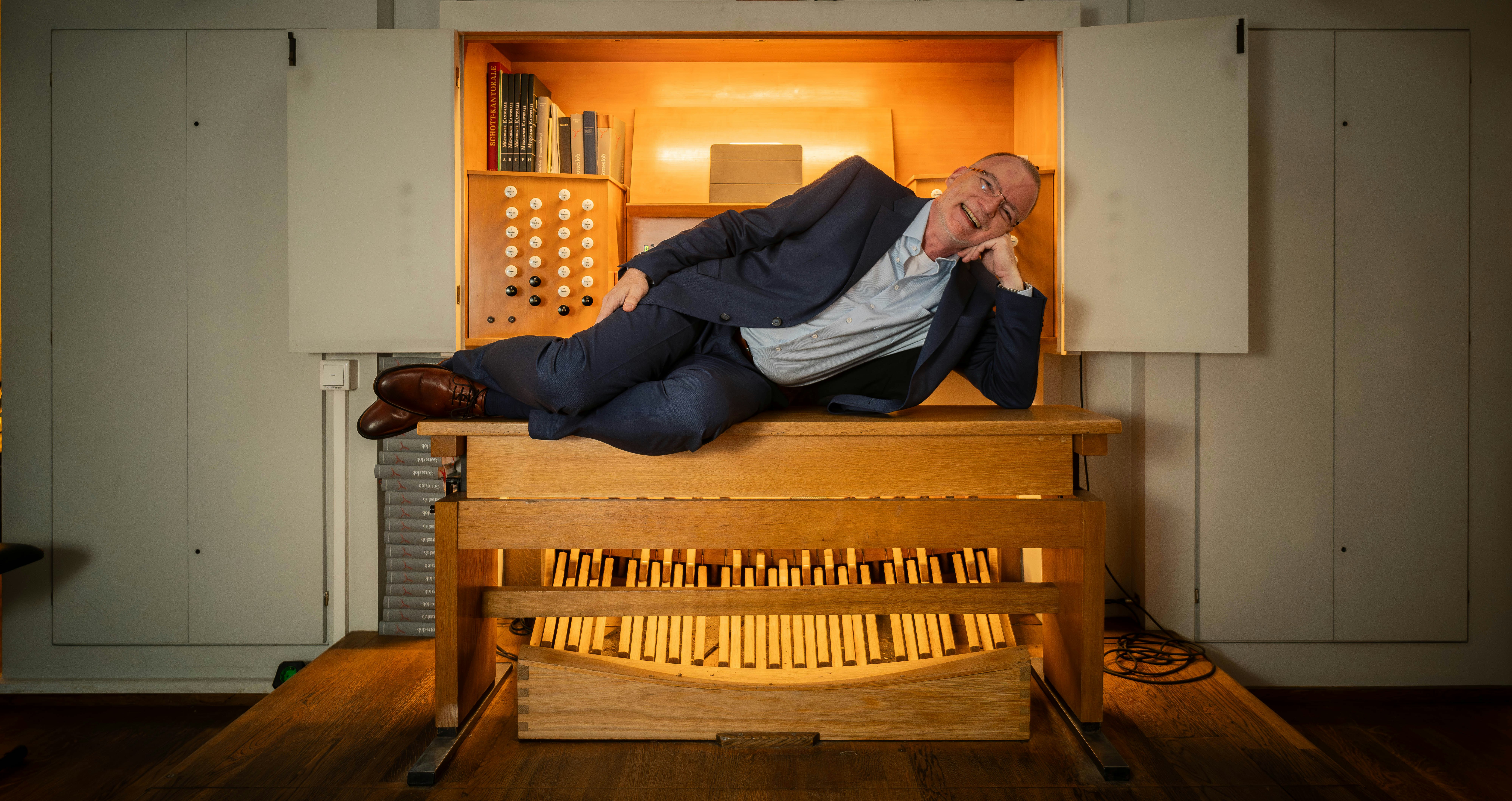 Matthias lies on a church organ bench wearing a suit.