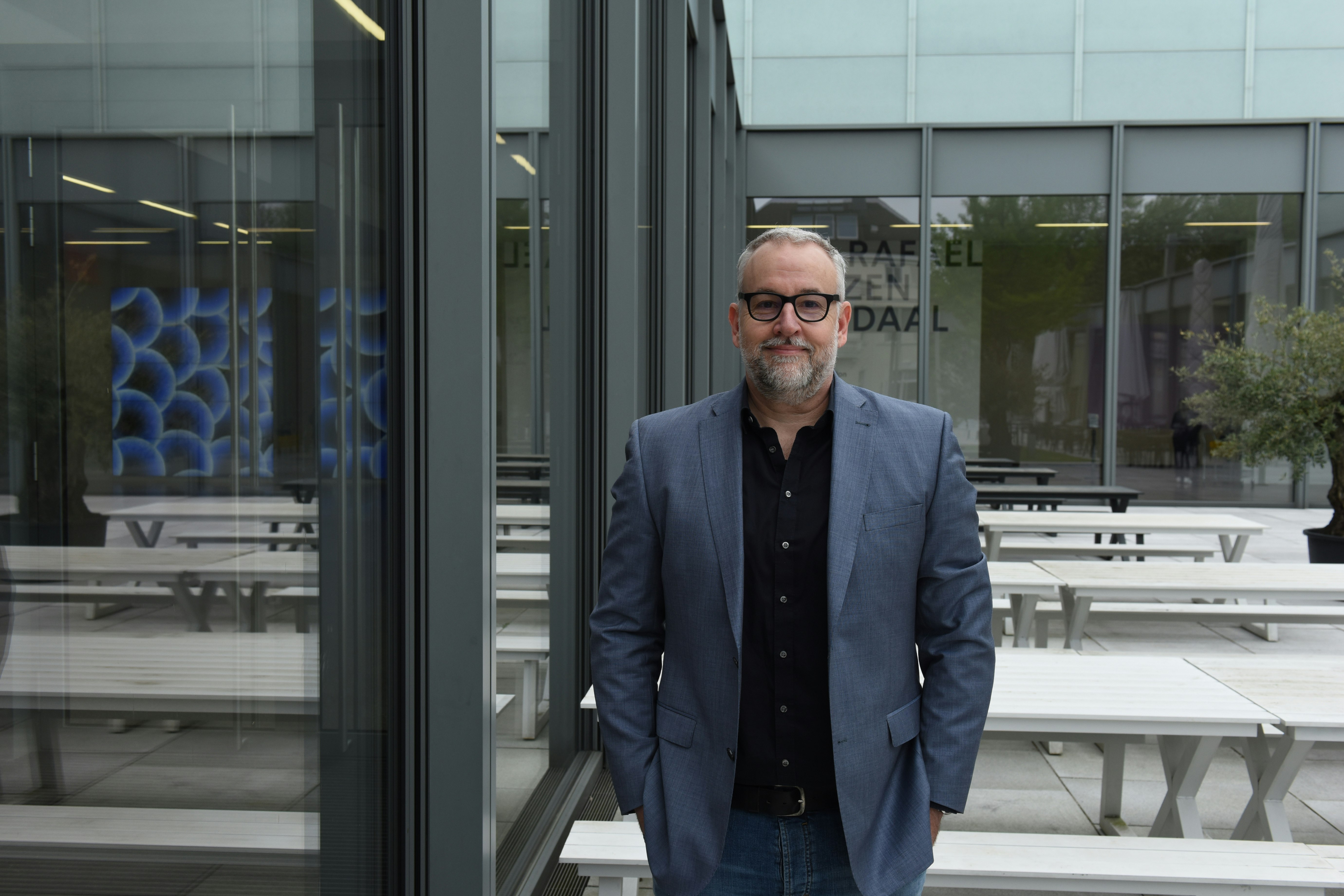 Marco standing in front of a grey building with grey jacket
