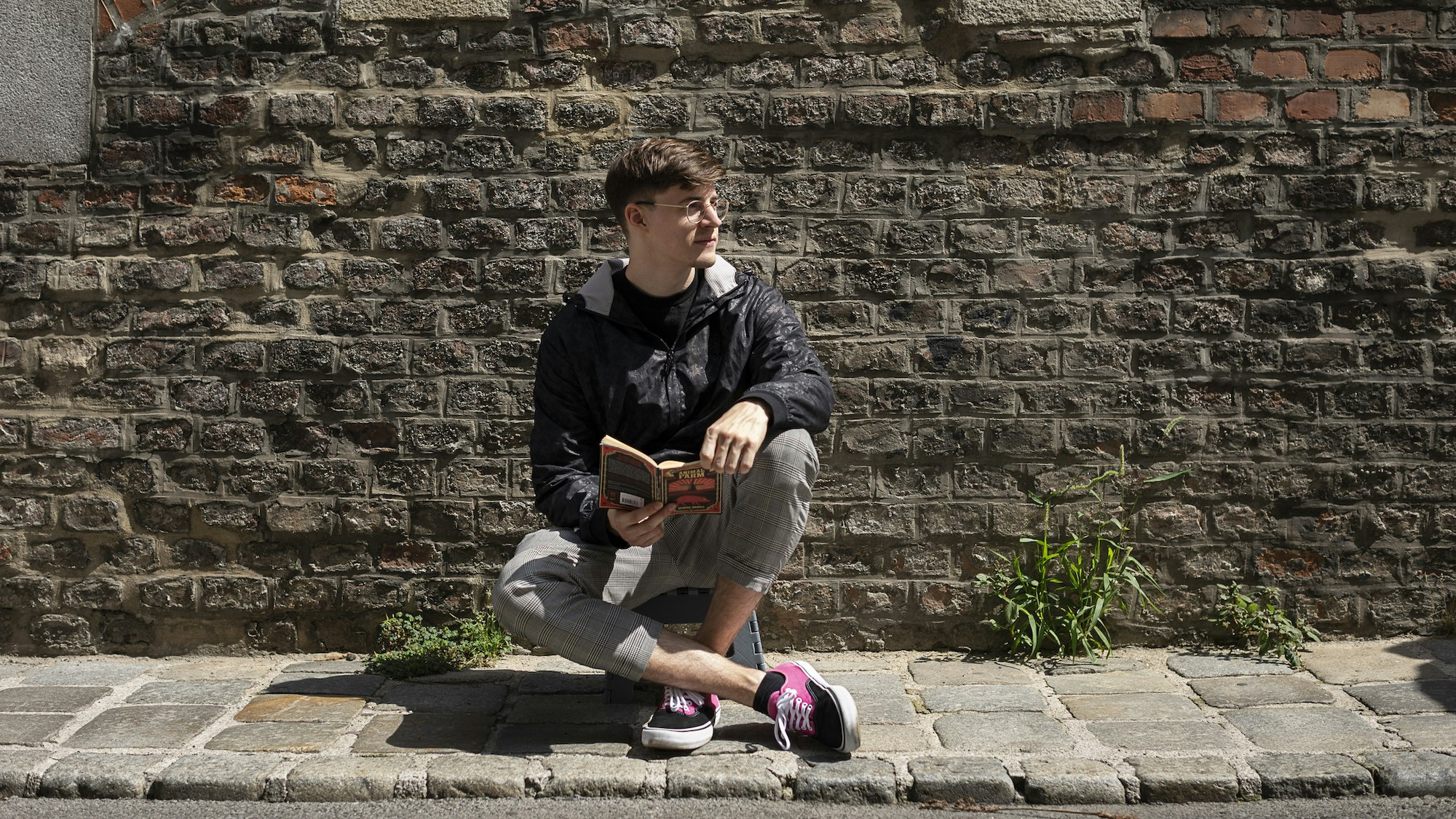 Christoph is sitting in front of an old brick wall with a book in his hand.