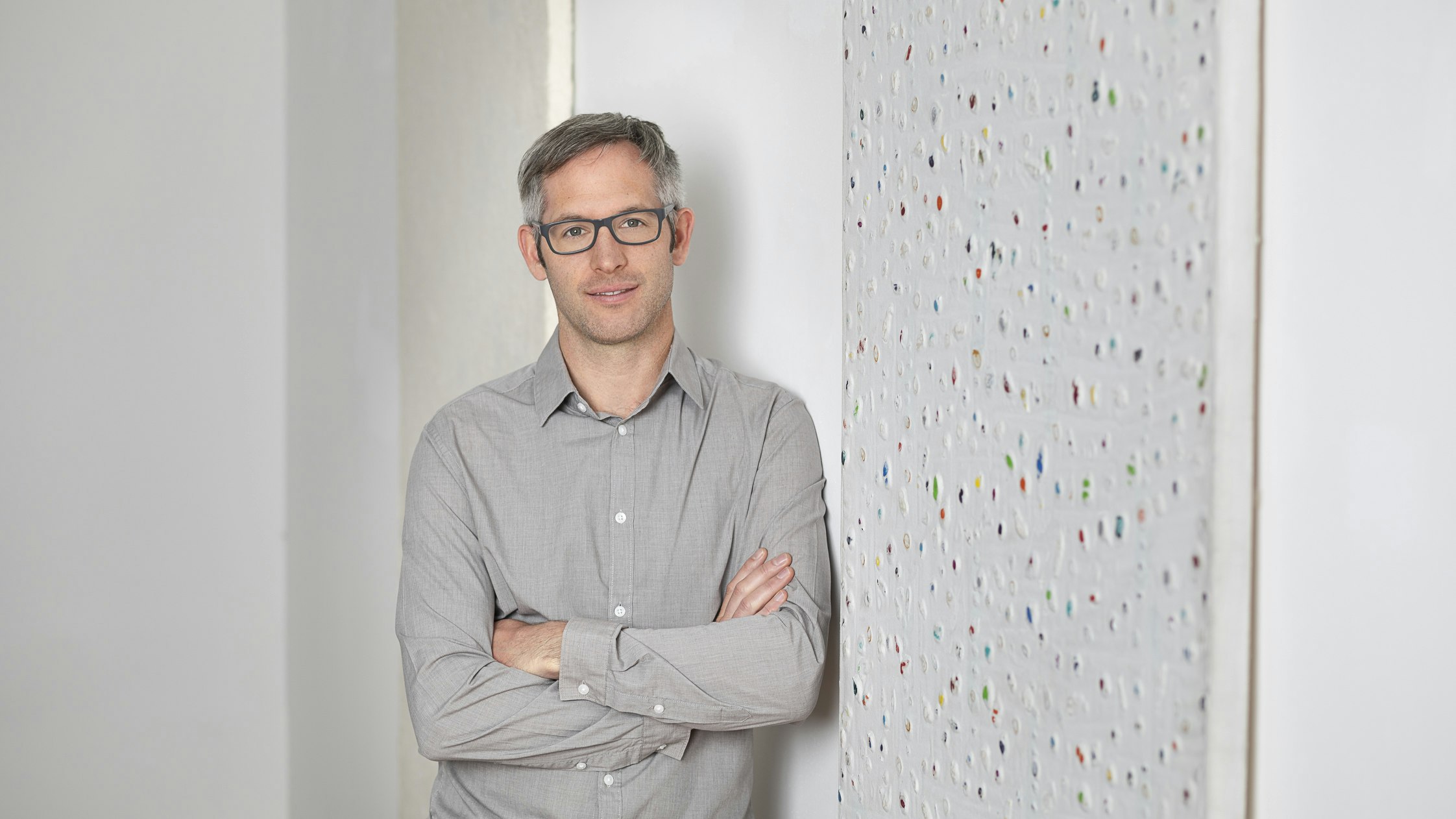 Dietmar leaning casually in front of a white work of art in the office.