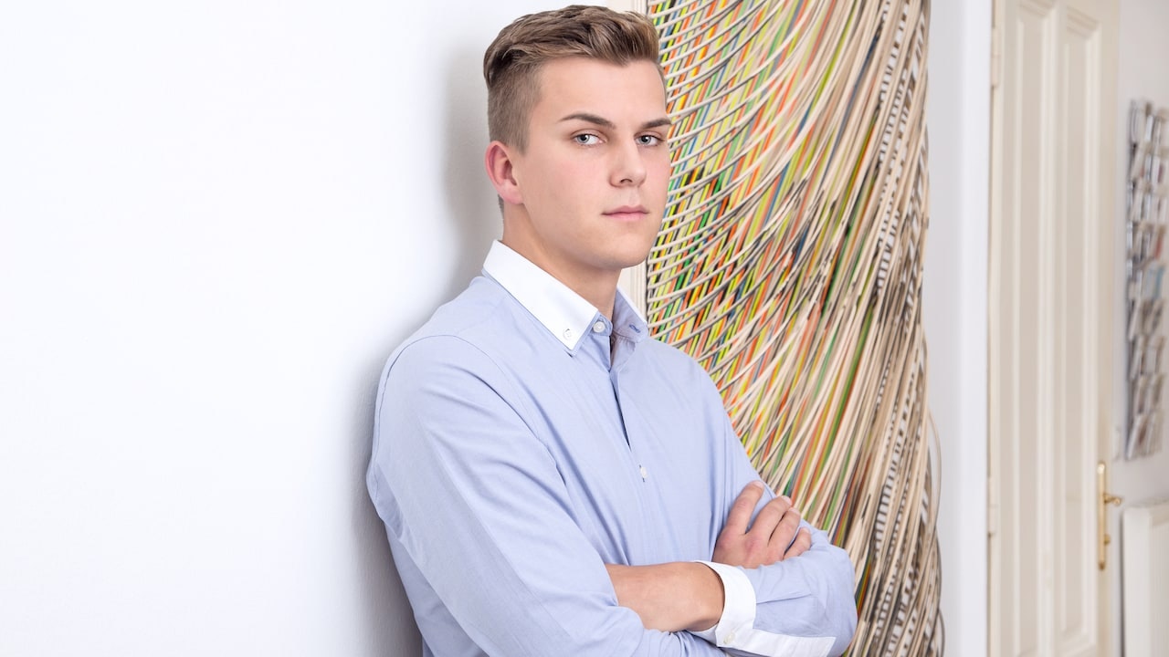 Julian lehnt an einer Wand, im Hintergrund hängt ein Kunstwerk.