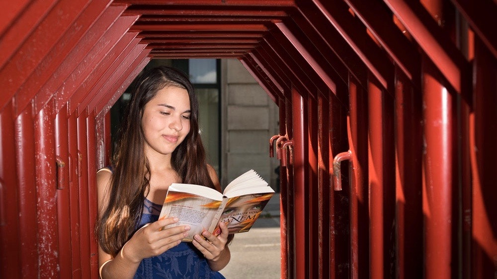 Sabine reads a book while standing under a sculpture made of red steel tubes.