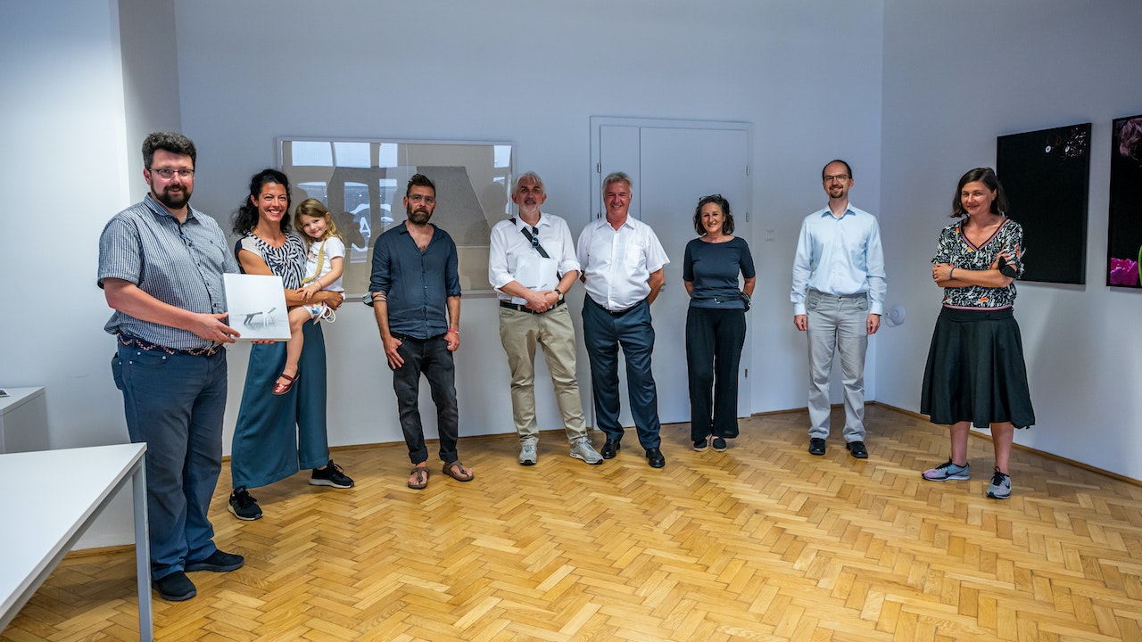 alle Beteiligten stehen im Halbkreis, im Hintergrund hängen die Kunstwerke an der Wand.